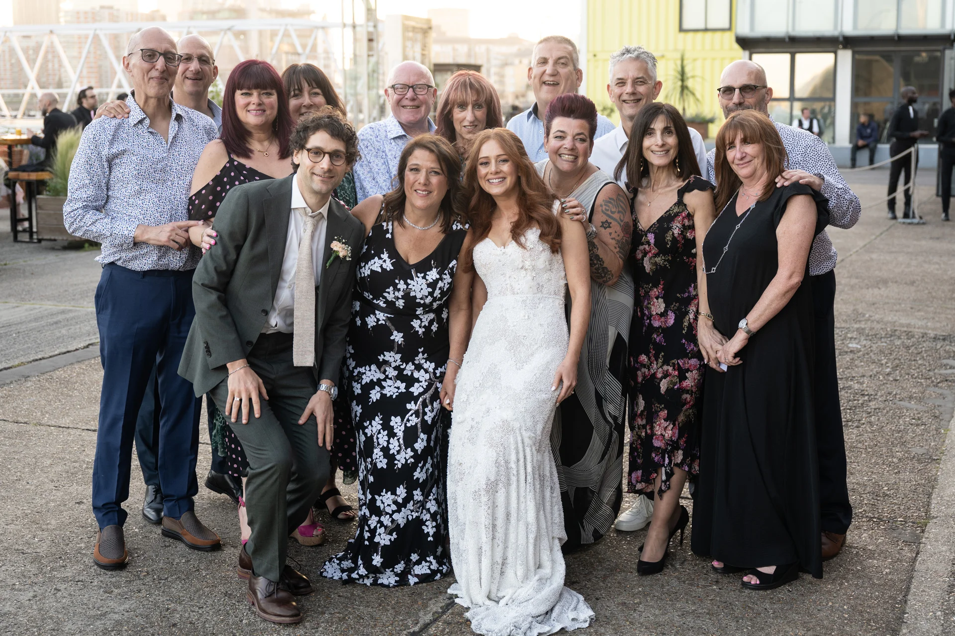 A happy bride and groom pose outdoors with family and friends during a relaxed summer wedding celebration.
