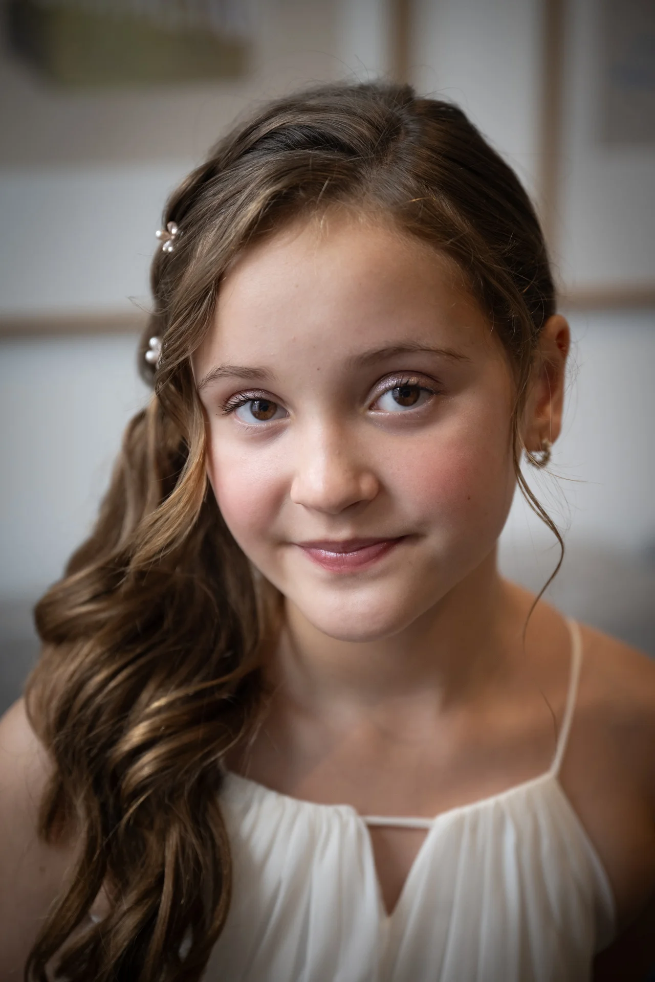 Close-up portrait of a young flower girl smiling gently with soft waves and delicate pearls in her hair.