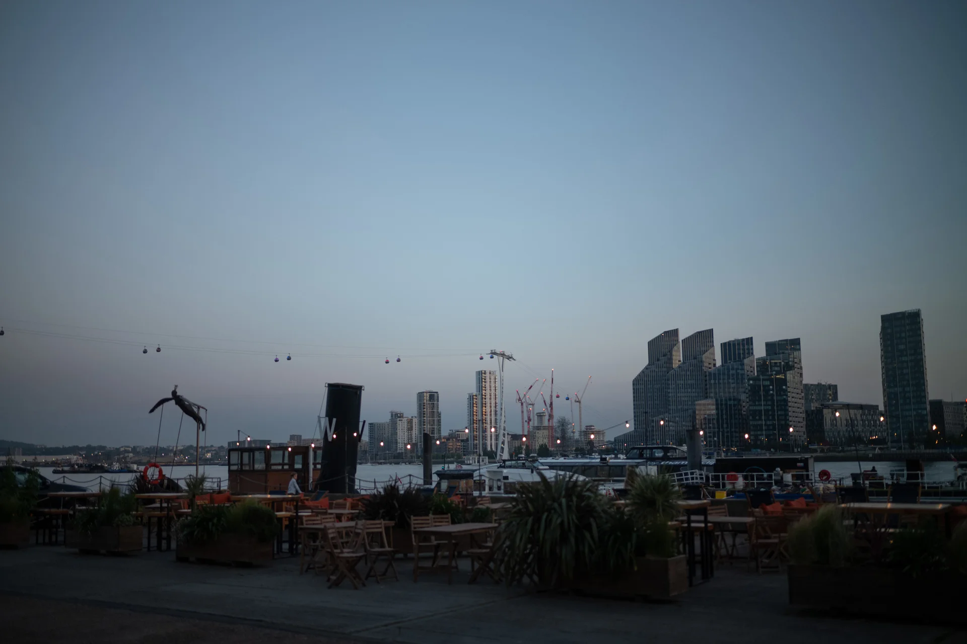 An atmospheric blue hour view of an outdoor urban wedding venue terrace overlooking a city skyline and waterfront.