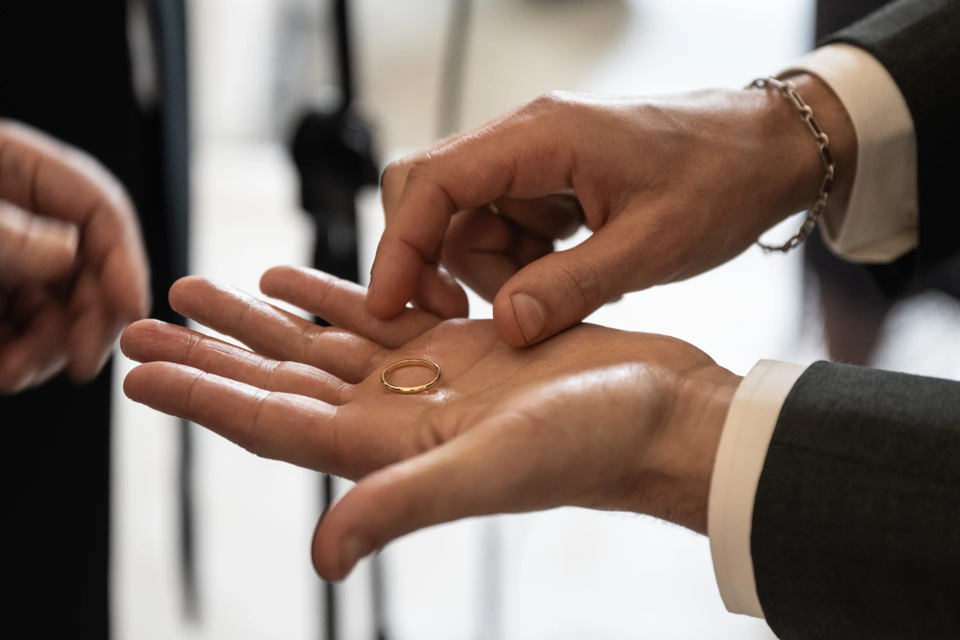 A close-up shot captures a gold wedding ring resting in the palm of a hand during a wedding ceremony.