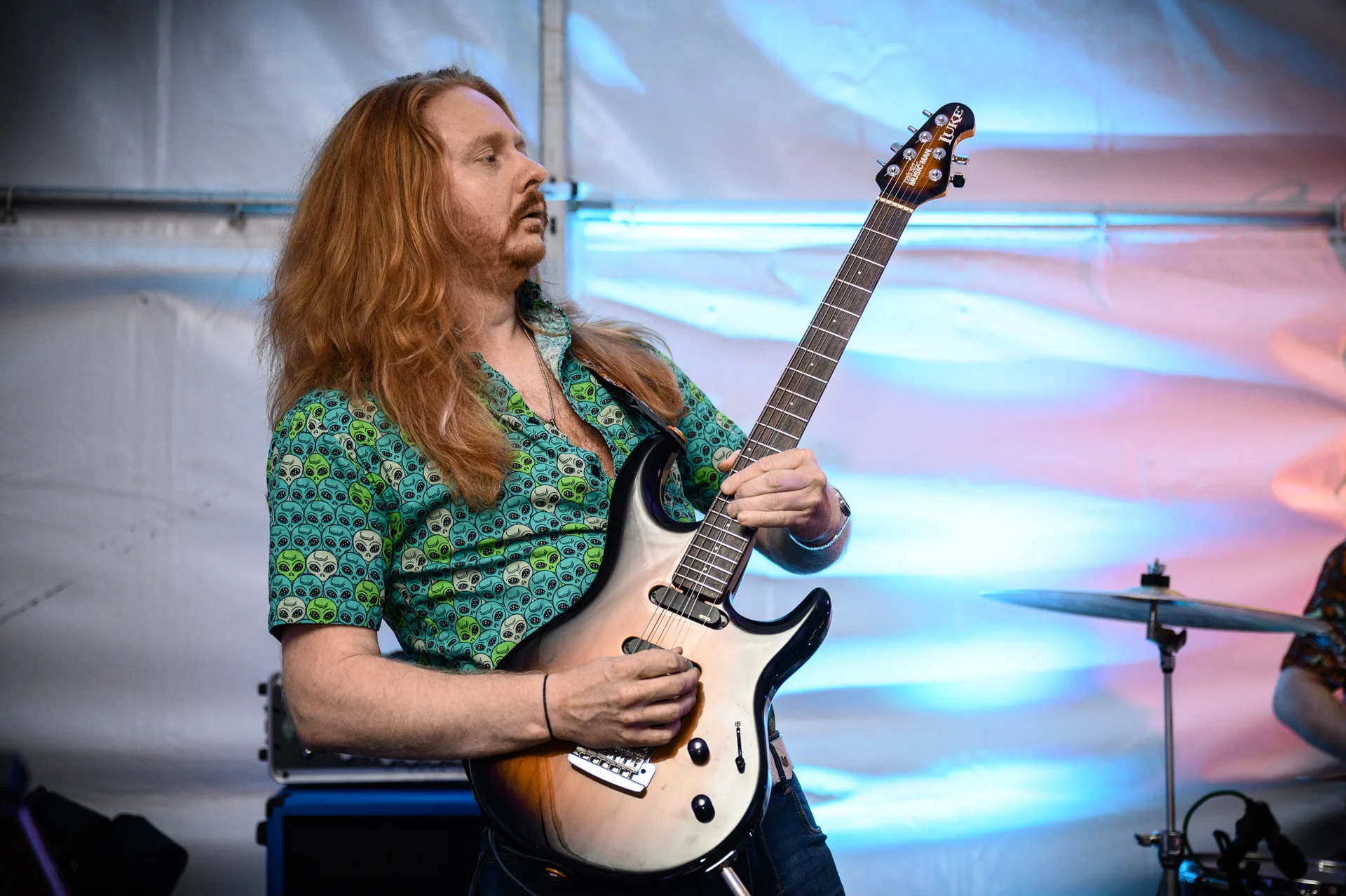 A long-haired musician plays an electric guitar passionately on stage under dynamic blue and white lighting during a wedding evening reception.