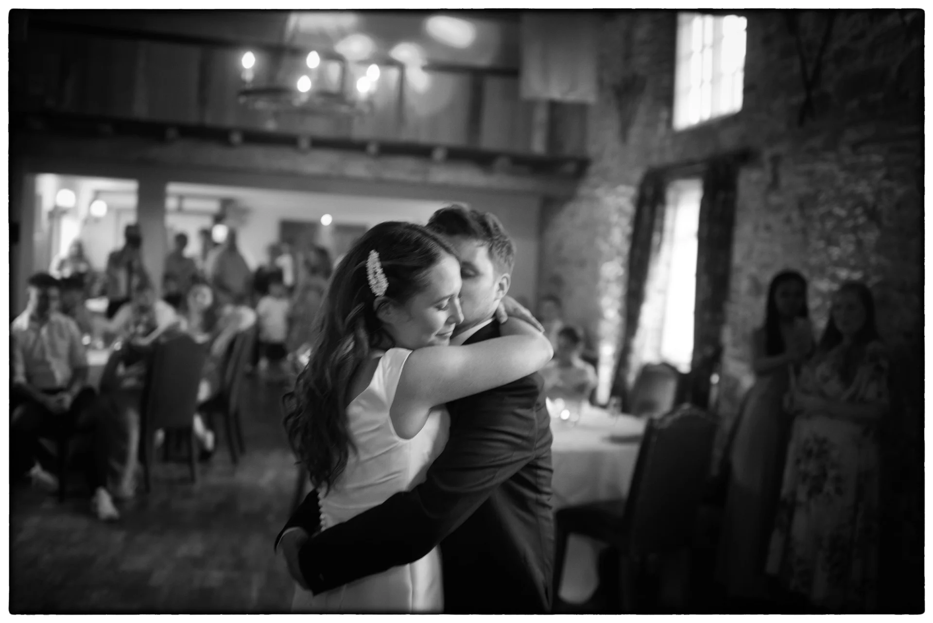 Newlyweds share an intimate embrace and forehead kiss during their first dance inside a rustic stone barn venue surrounded by guests.