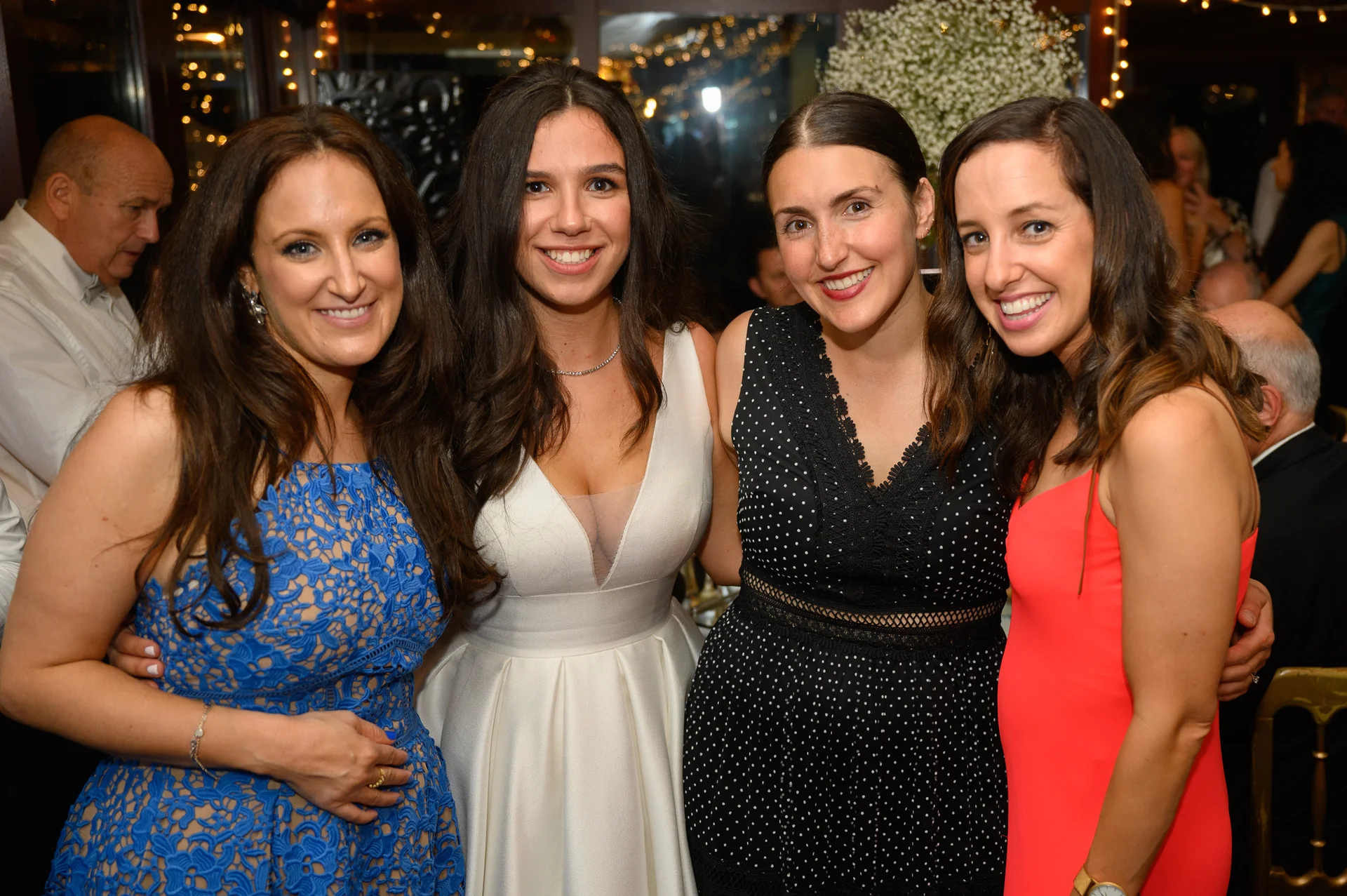 Four smiling guests pose together inside a warmly lit venue adorned with twinkling fairy lights.