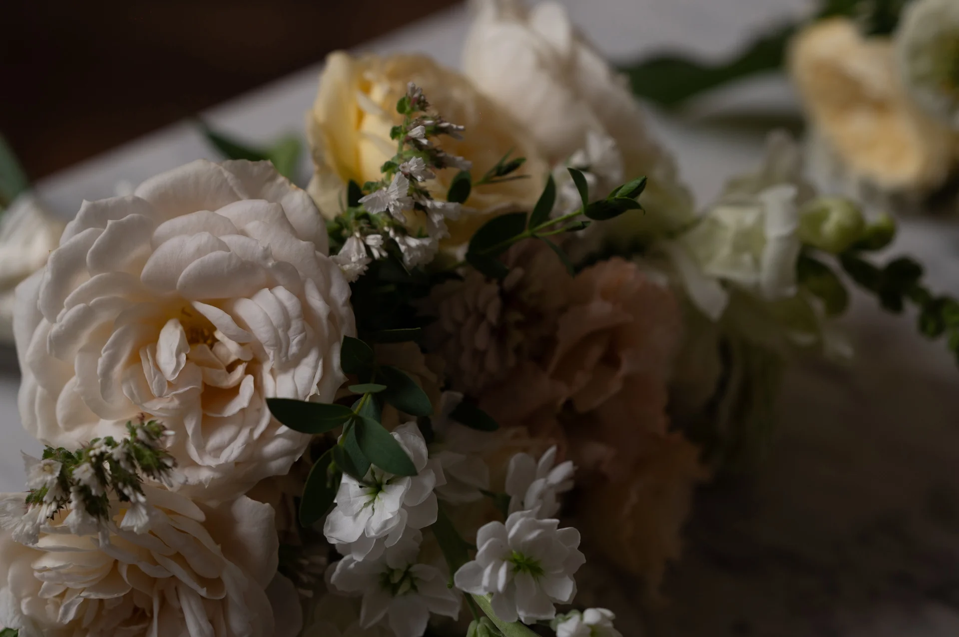 A close-up view of a romantic wedding bouquet featuring cream roses, delicate white stocks, and fresh eucalyptus foliage.