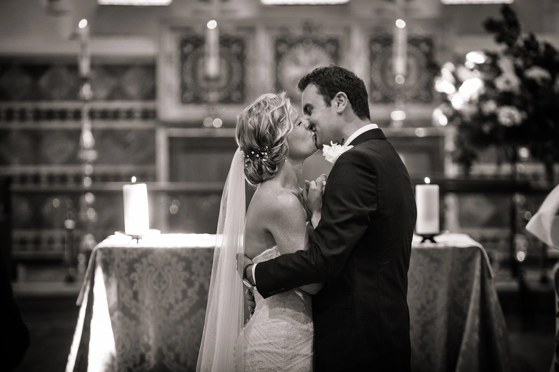 A newlywed couple share their first kiss at the altar during a candlelit church wedding ceremony.