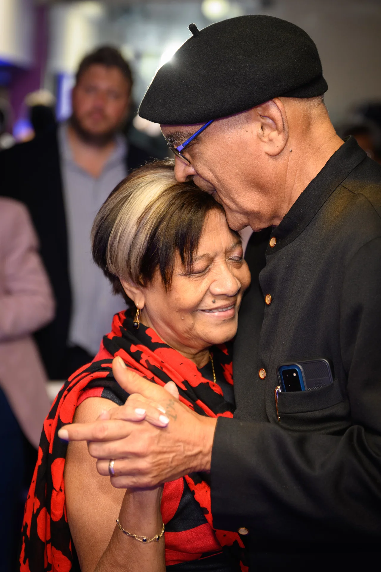 An older couple shares a tender moment while dancing, with the man gently kissing the woman's forehead during the wedding reception.
