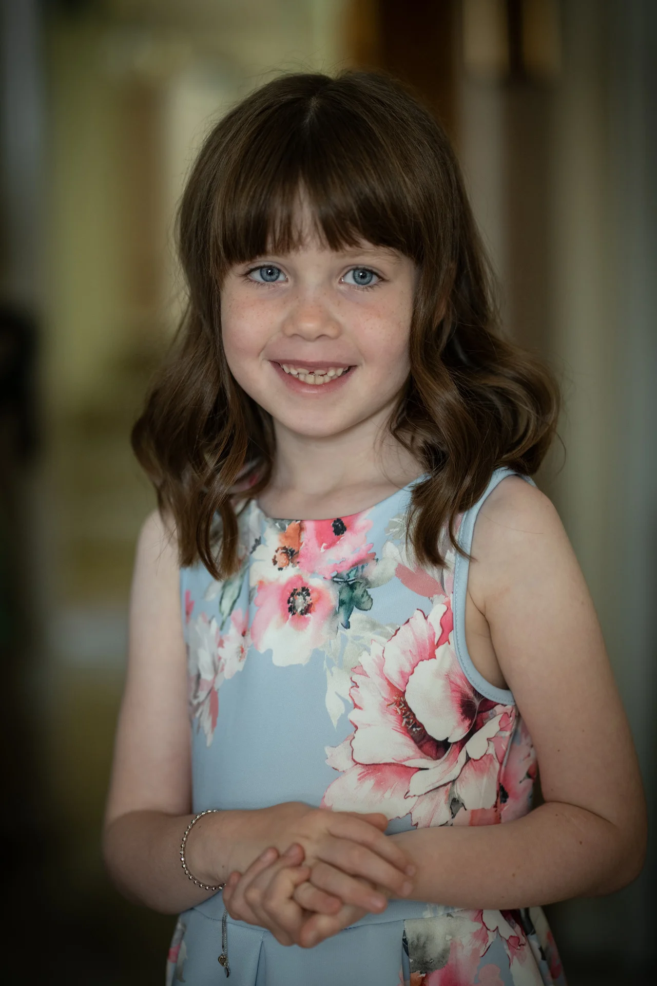 A young flower girl smiles warmly for a portrait while wearing a light blue floral dress with pink blossoms.