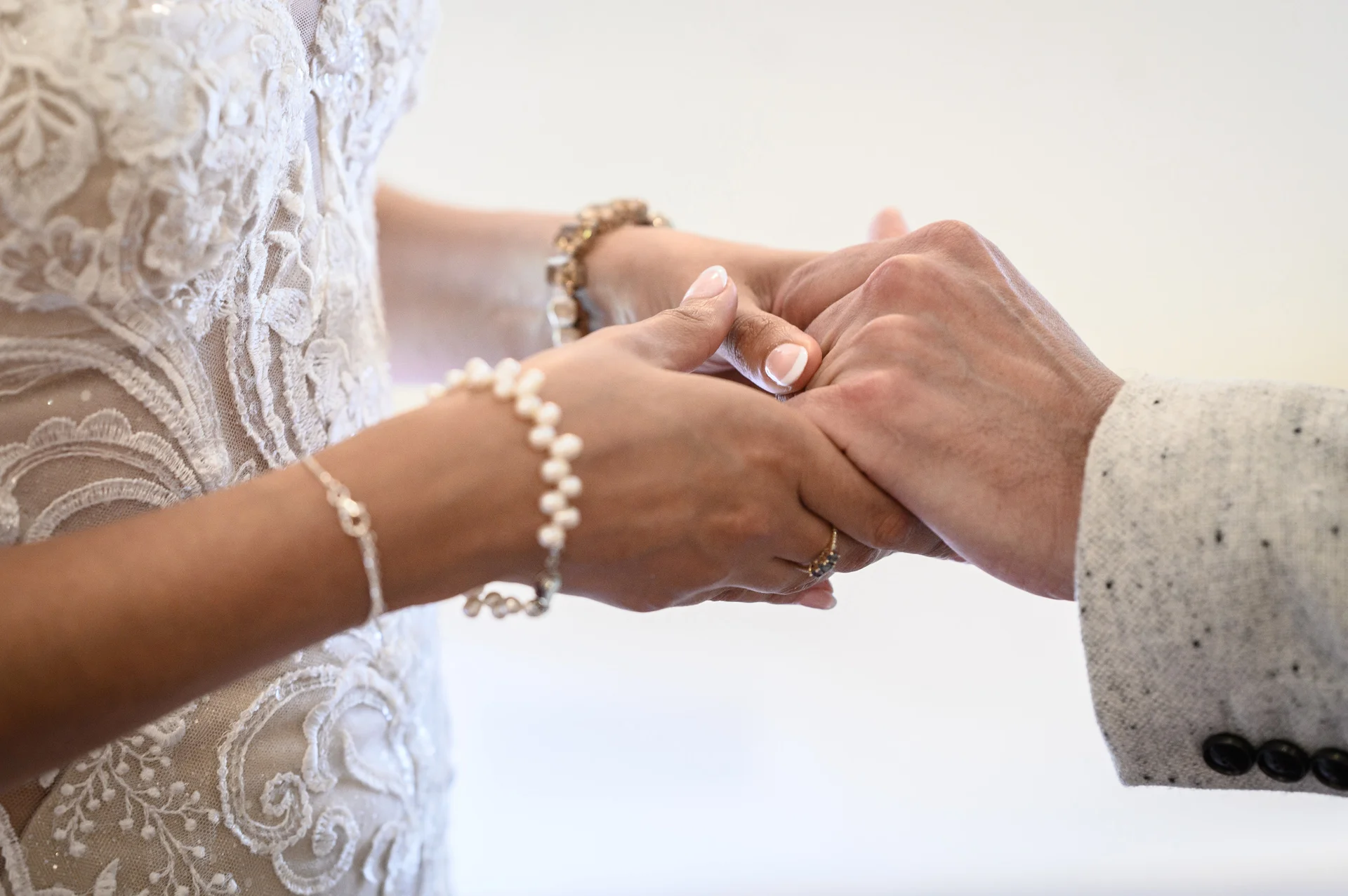 Close-up of a bride wearing a lace wedding dress and pearl bracelet holding hands tenderly with the groom.