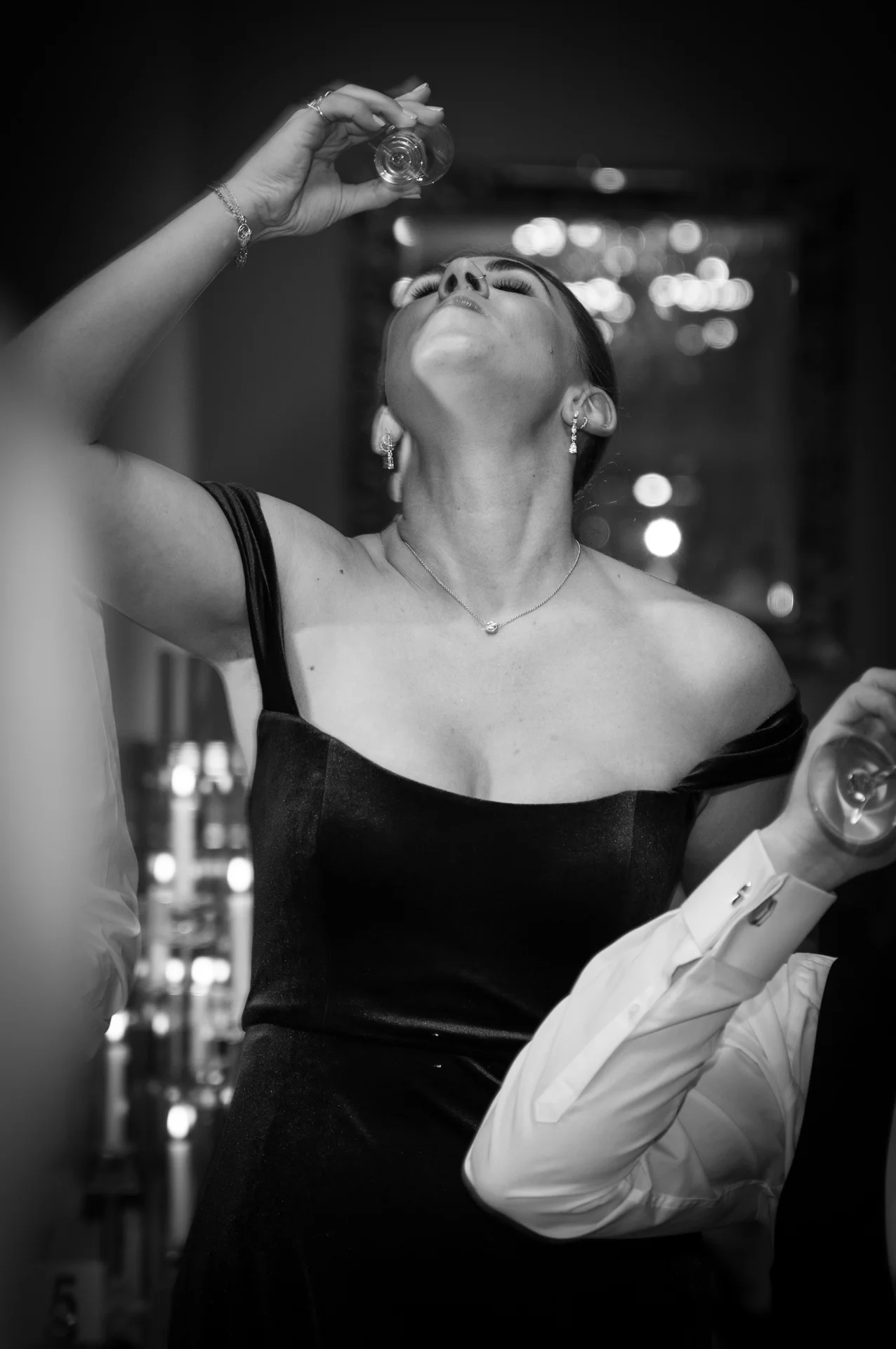 A guest in a black velvet off-the-shoulder dress leans back to take a shot during the evening party reception.