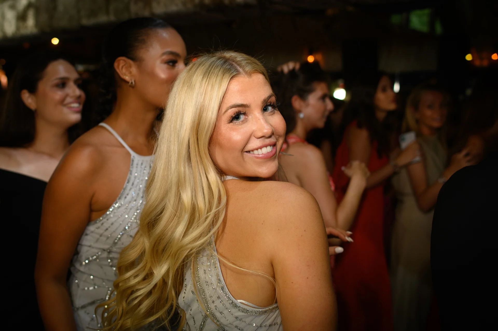 A blonde guest smiles over her shoulder on a lively evening dance floor surrounded by friends.