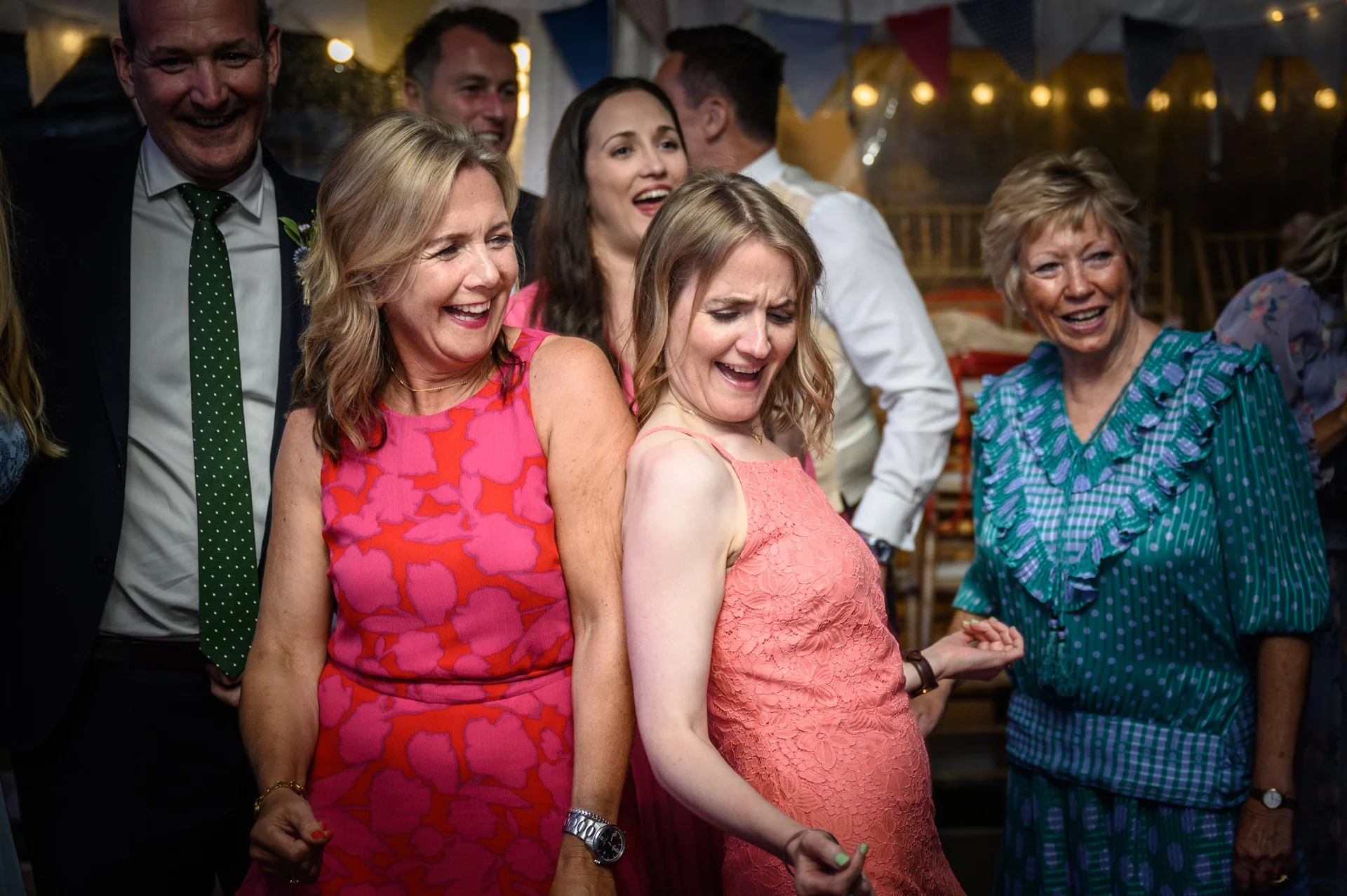 Wedding guests laughing and dancing together during the lively evening reception under festoon lighting.