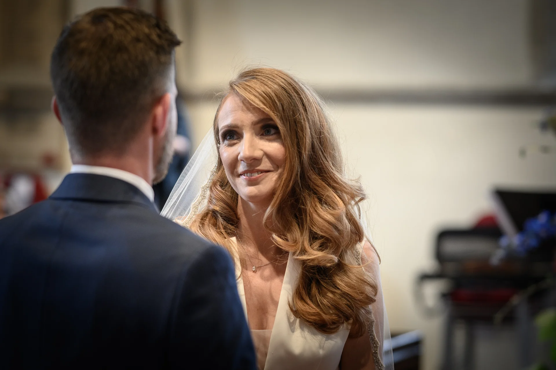 The bride gazes lovingly at the groom over his shoulder with a tender smile during their wedding ceremony.