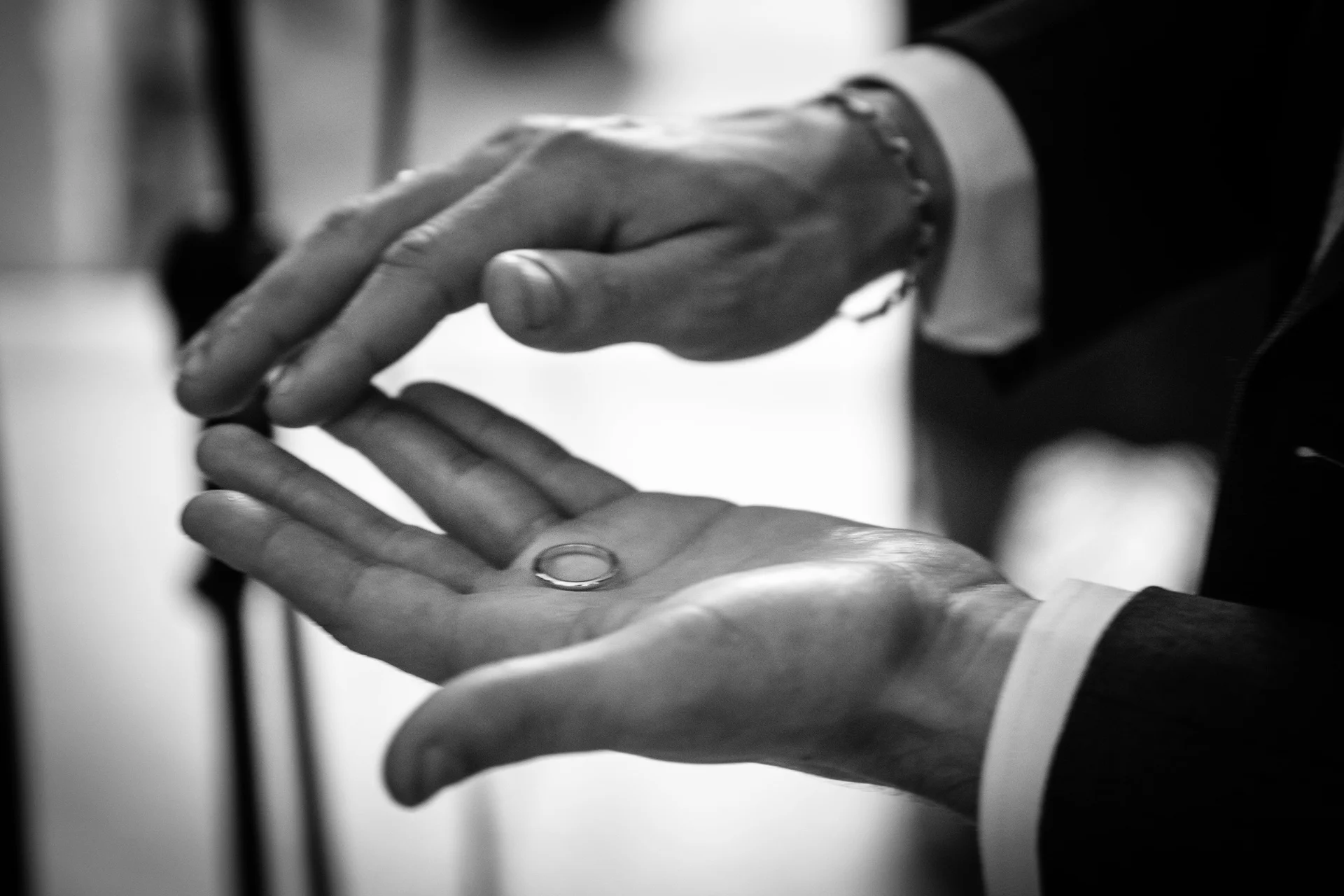 A black and white macro shot capturing a wedding ring resting delicately in the palm of a hand during the ceremony.