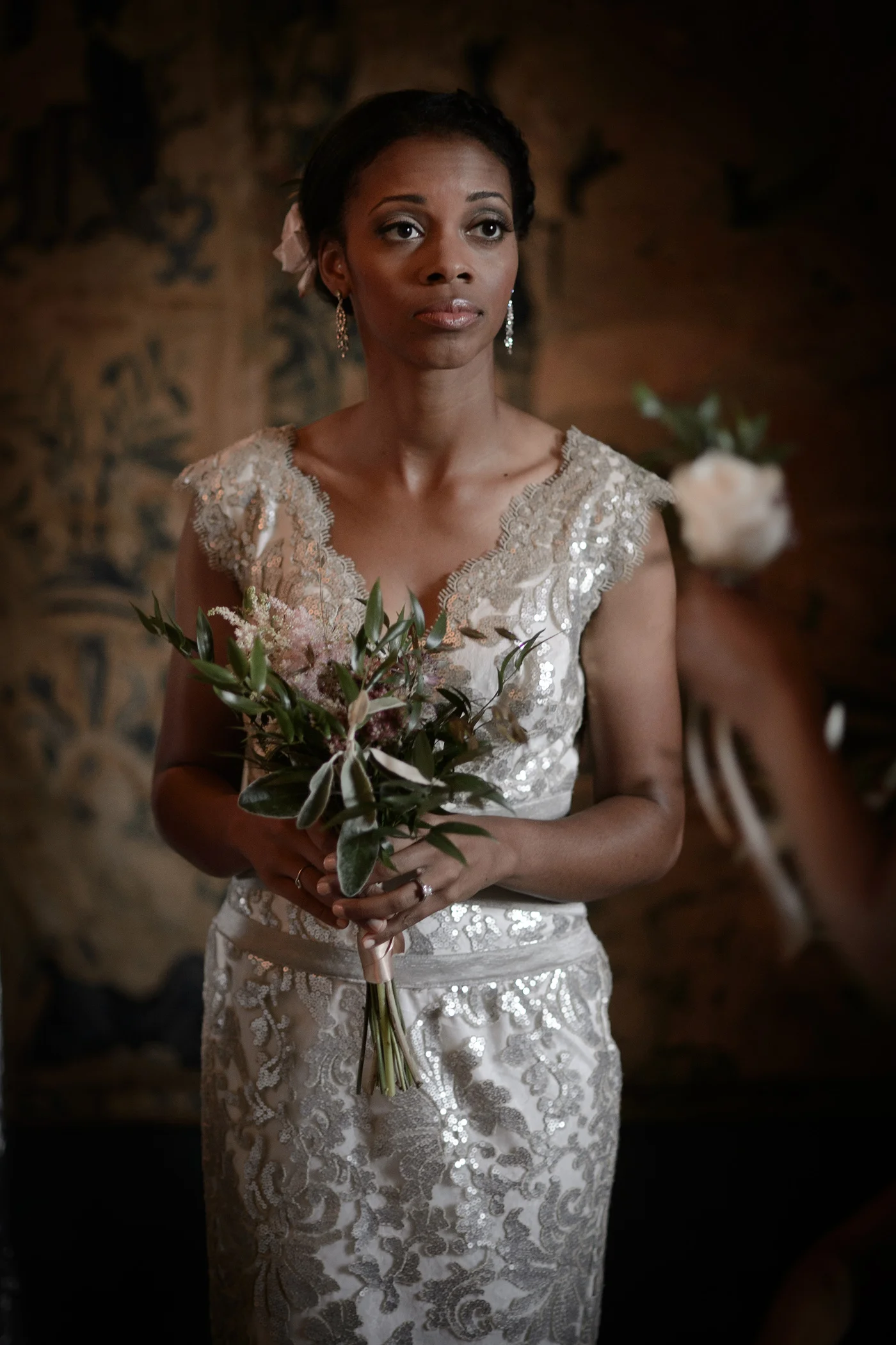 A stunning black bride in a shimmering sequin and lace wedding dress holding a rustic bouquet indoors with moody lighting.