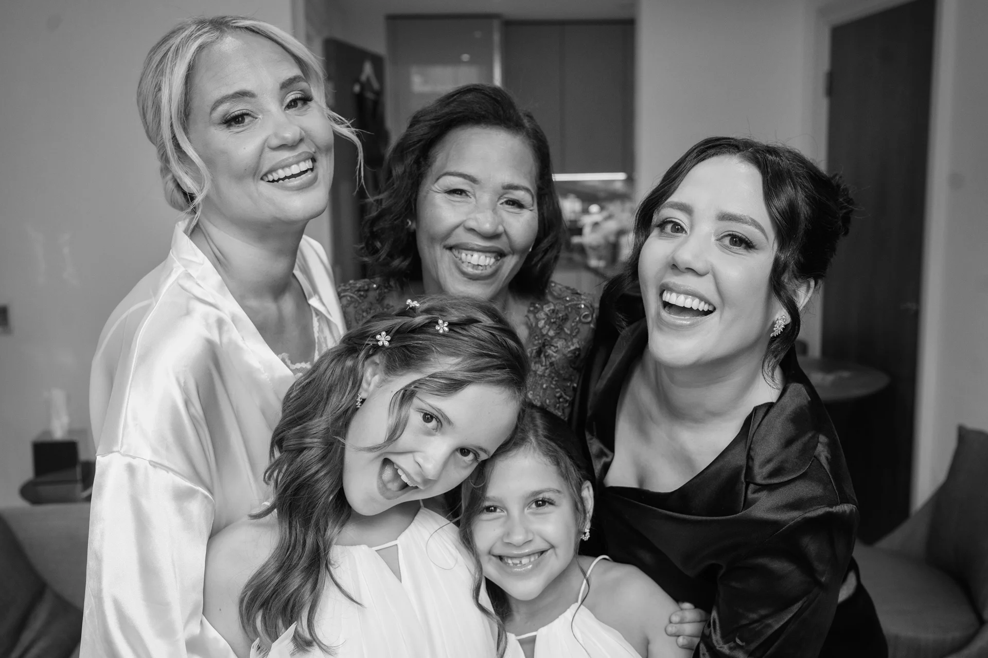 A joyful black and white portrait captures a multi-generational group of women and young girls laughing together while getting ready in matching robes.