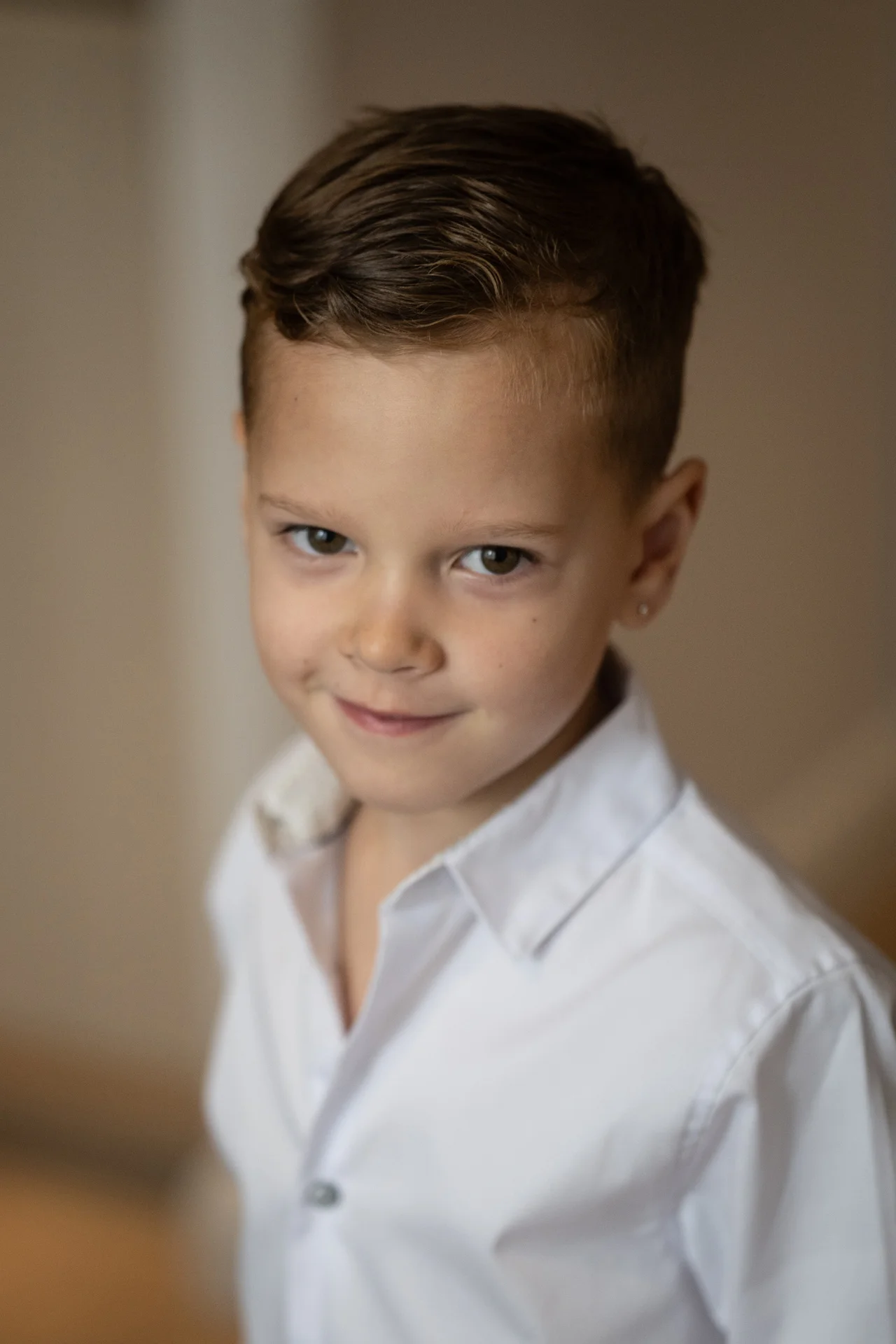 A young page boy dressed in a white collared shirt looks up towards the camera with a gentle, smiling expression.