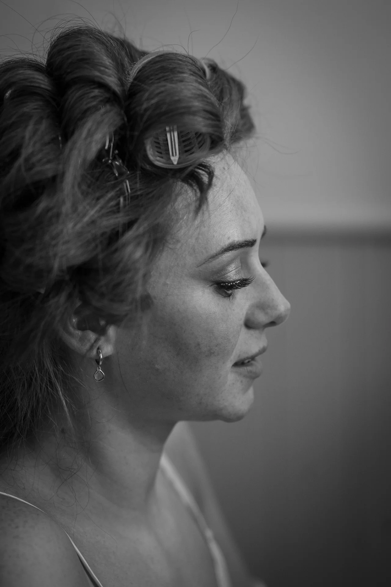 A close-up black and white profile shot of a bride with hair rollers in her hair getting ready on her wedding morning.