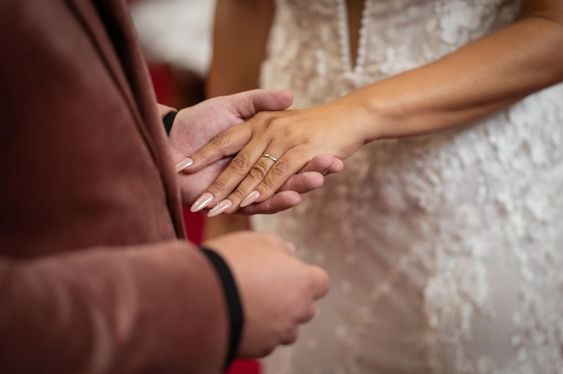 A close-up shot captures the tender moment during the ceremony as the couple gently hold hands and showcase their new wedding band.