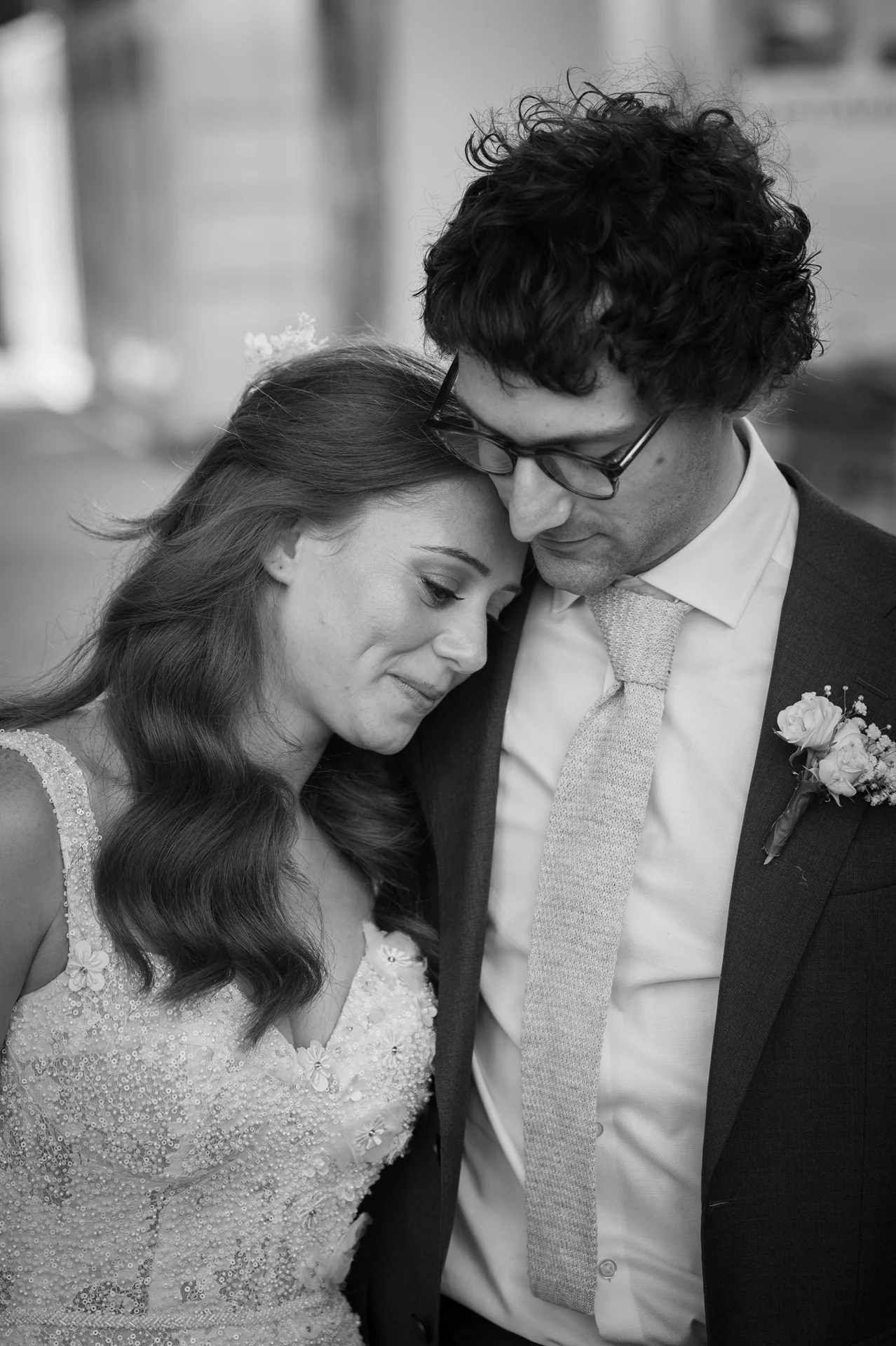 A tender black and white portrait of a bride resting her head gently on the groom's shoulder while wearing an embellished beaded gown.