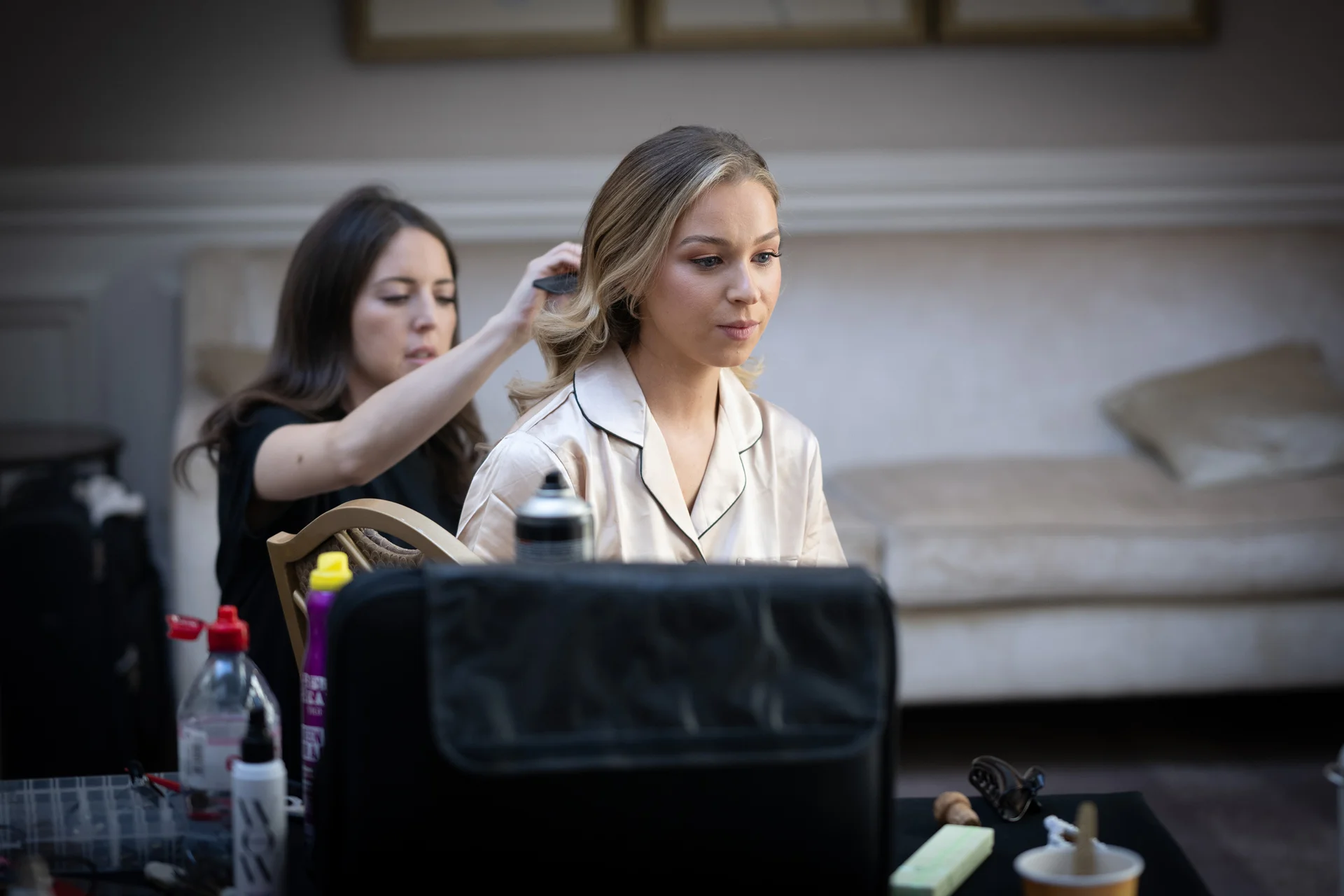A bride sits calmly while a hairstylist works on her blonde hair during bridal morning preparations.