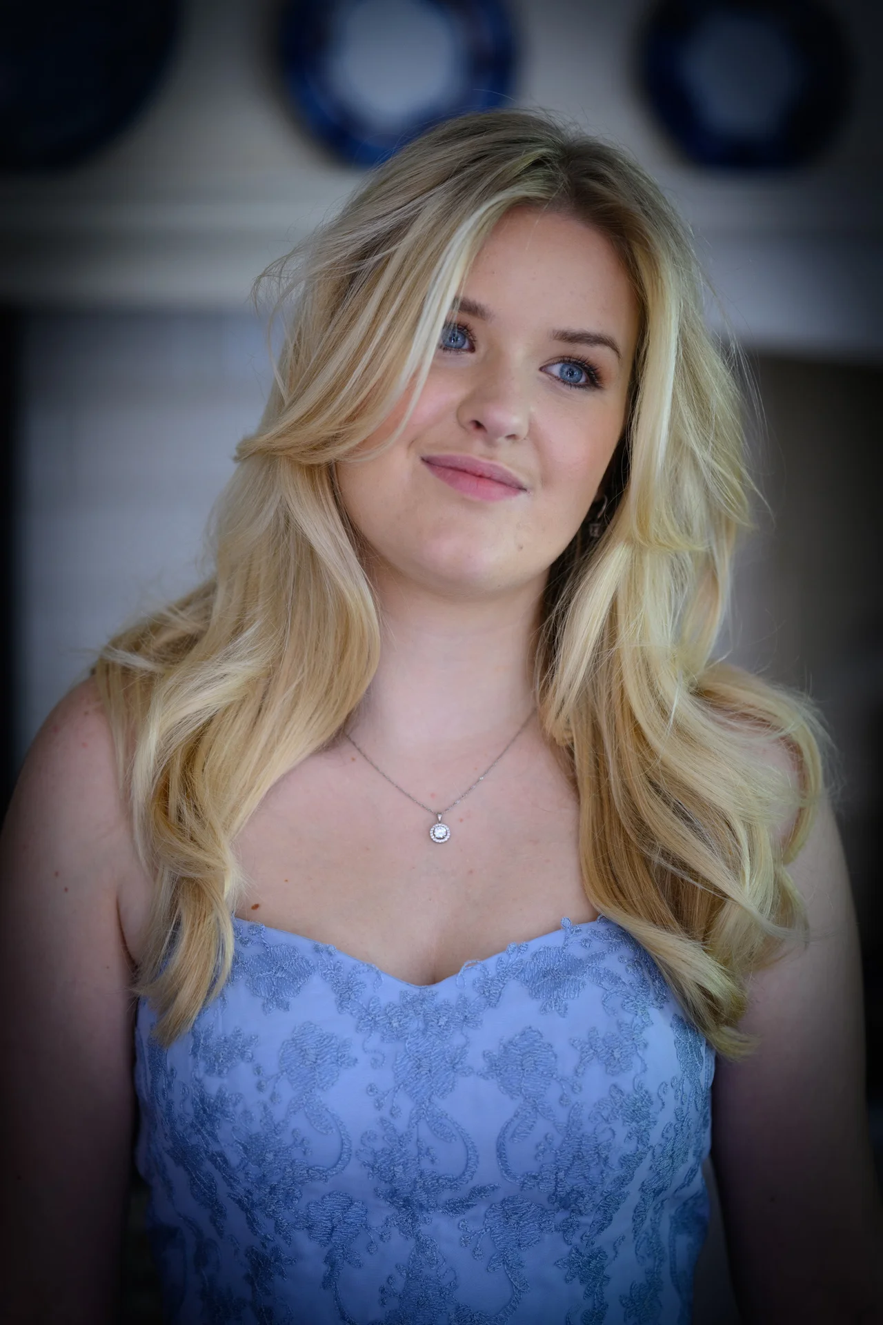 A close-up portrait of a blonde bride wearing a blue embroidered gown with a sweetheart neckline and a delicate pendant necklace.