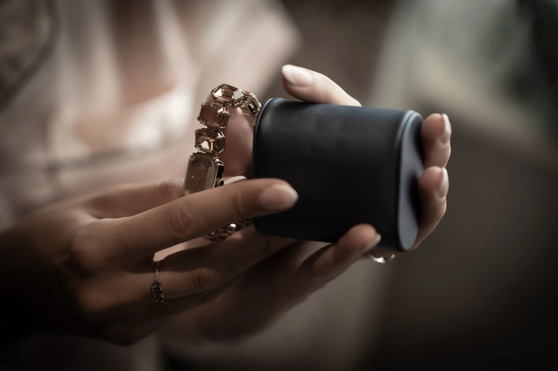 A close-up shot captures hands delicately holding a luxury watch against a dark leather case during wedding morning preparations.