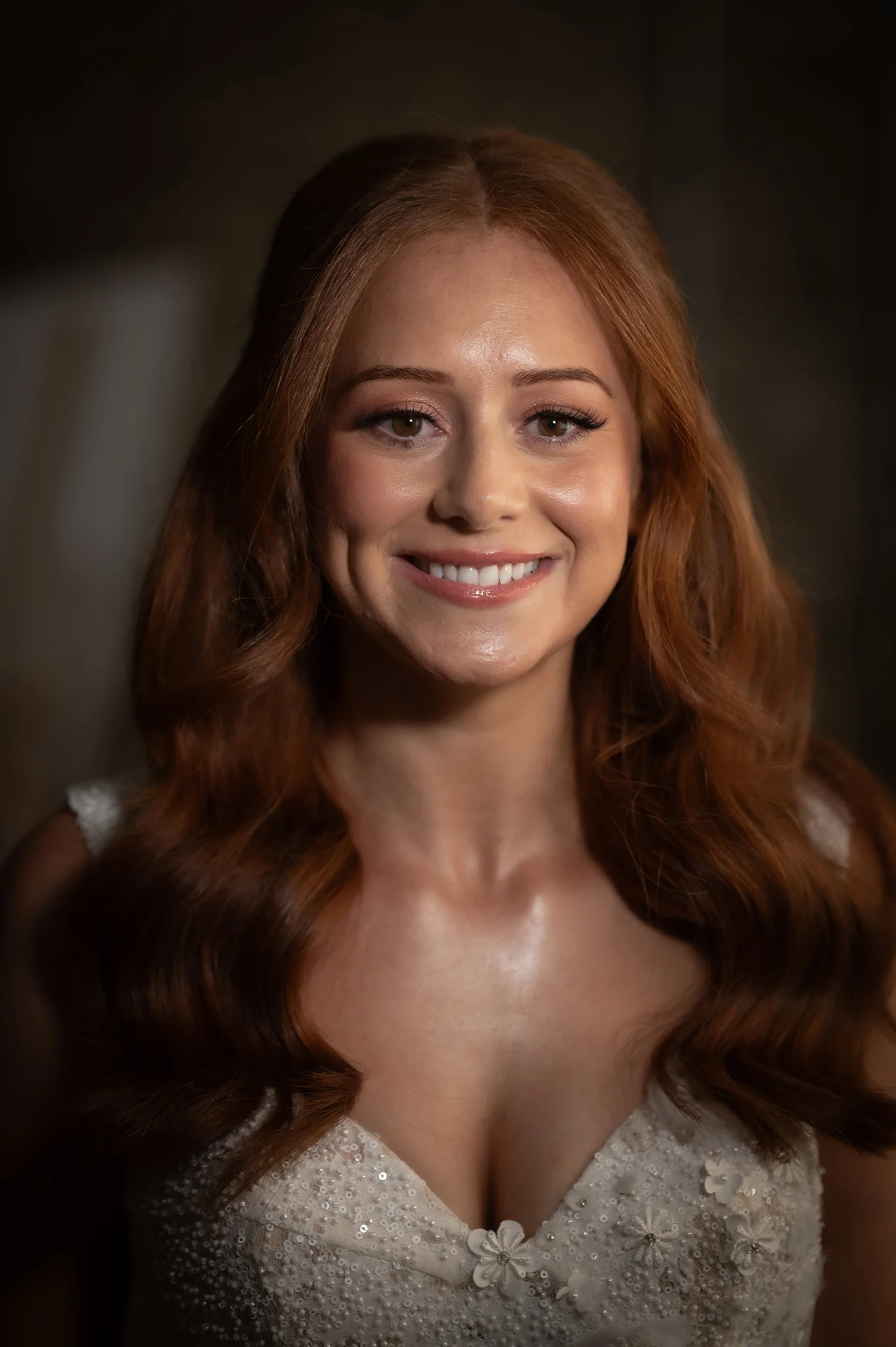 A stunning portrait of a smiling bride with flowing red hair in a half-up style, wearing a beaded V-neck gown with delicate floral appliques.