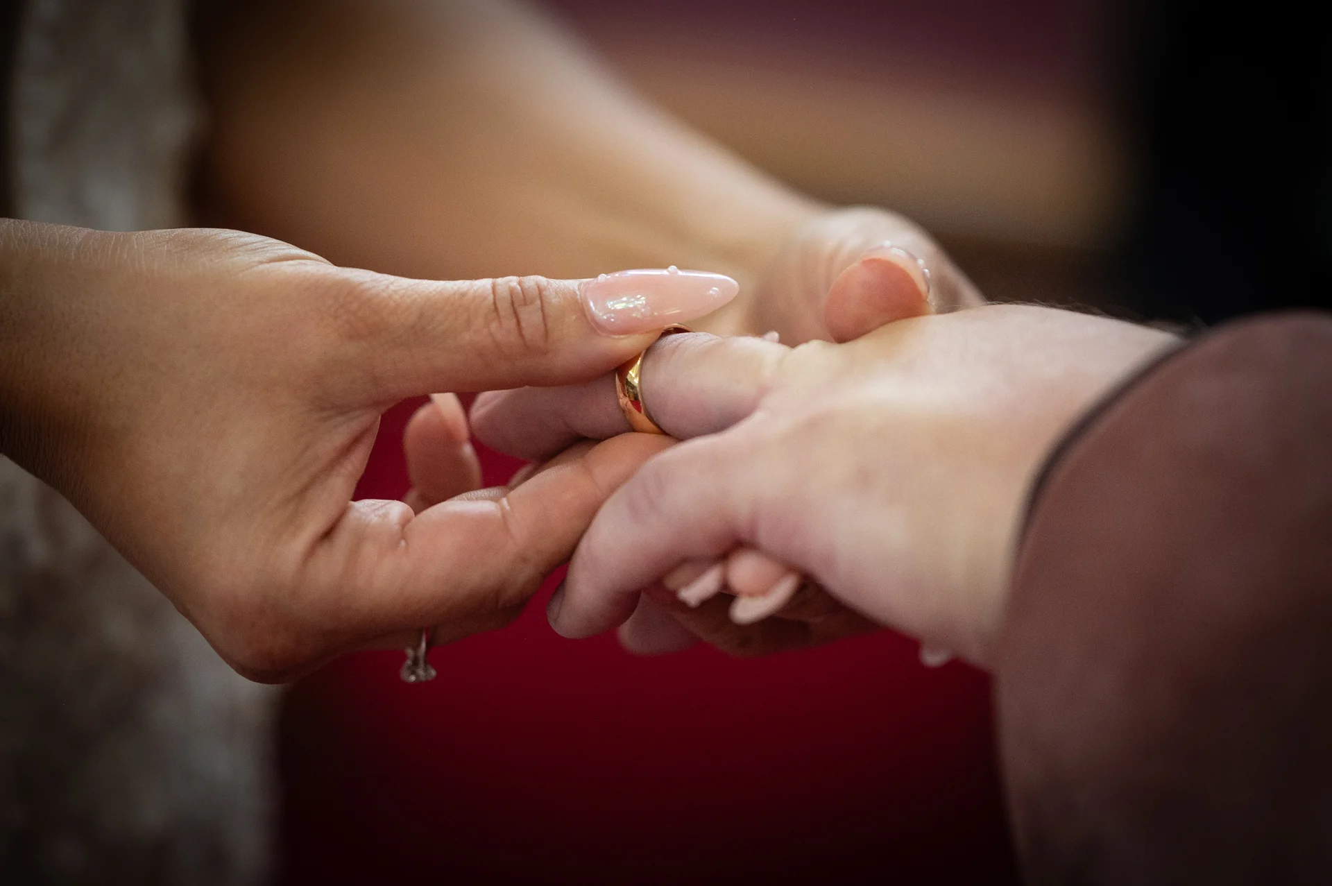 A close-up shot captures a partner carefully sliding a golden wedding band onto a finger during the ring exchange ceremony.