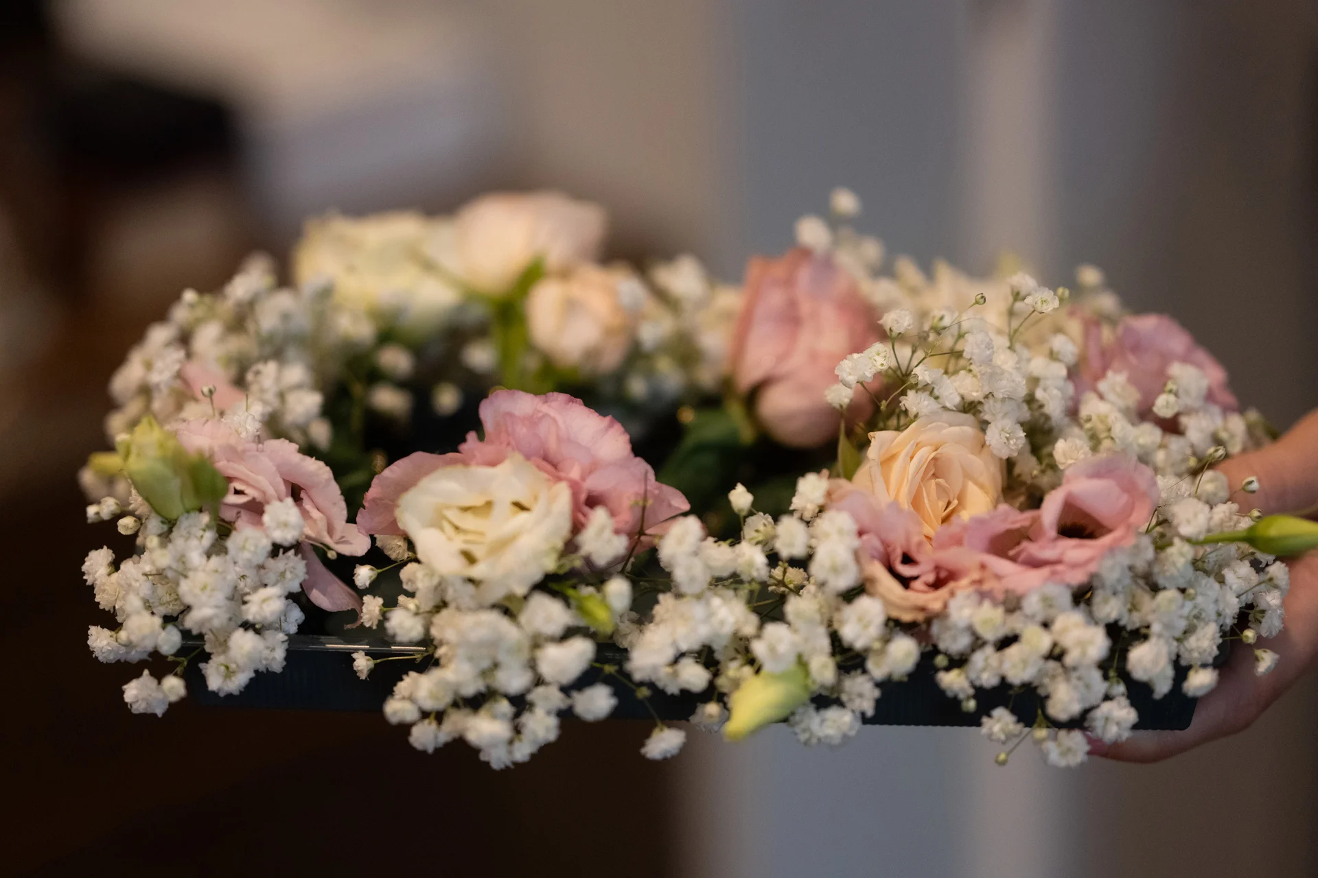 A delicate floral crown made of pink roses, white lisianthus, and abundant baby's breath is held up for display.
