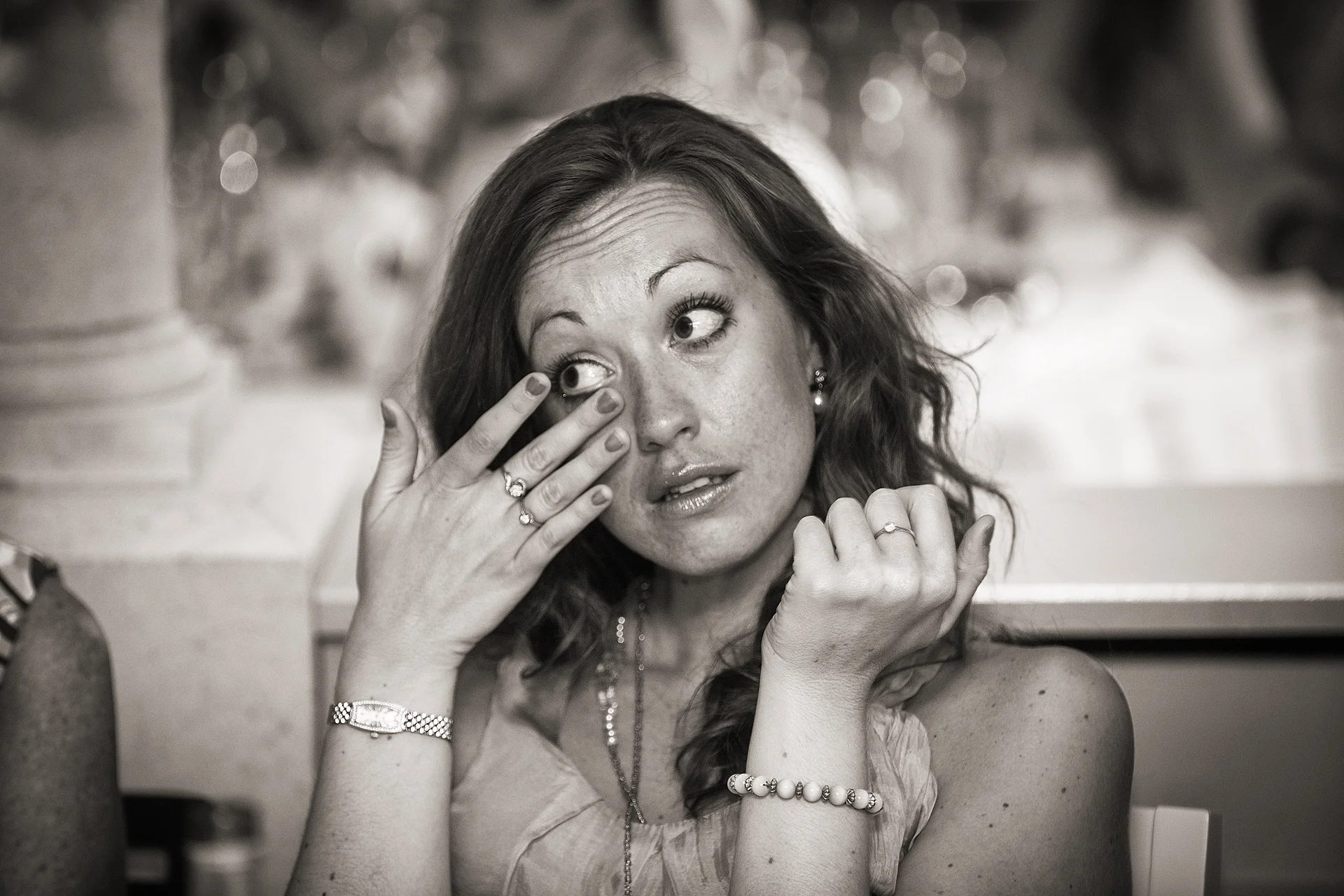 A guest is visibly moved to tears during wedding speeches, wiping her eye while wearing jewellery and a delicate dress.