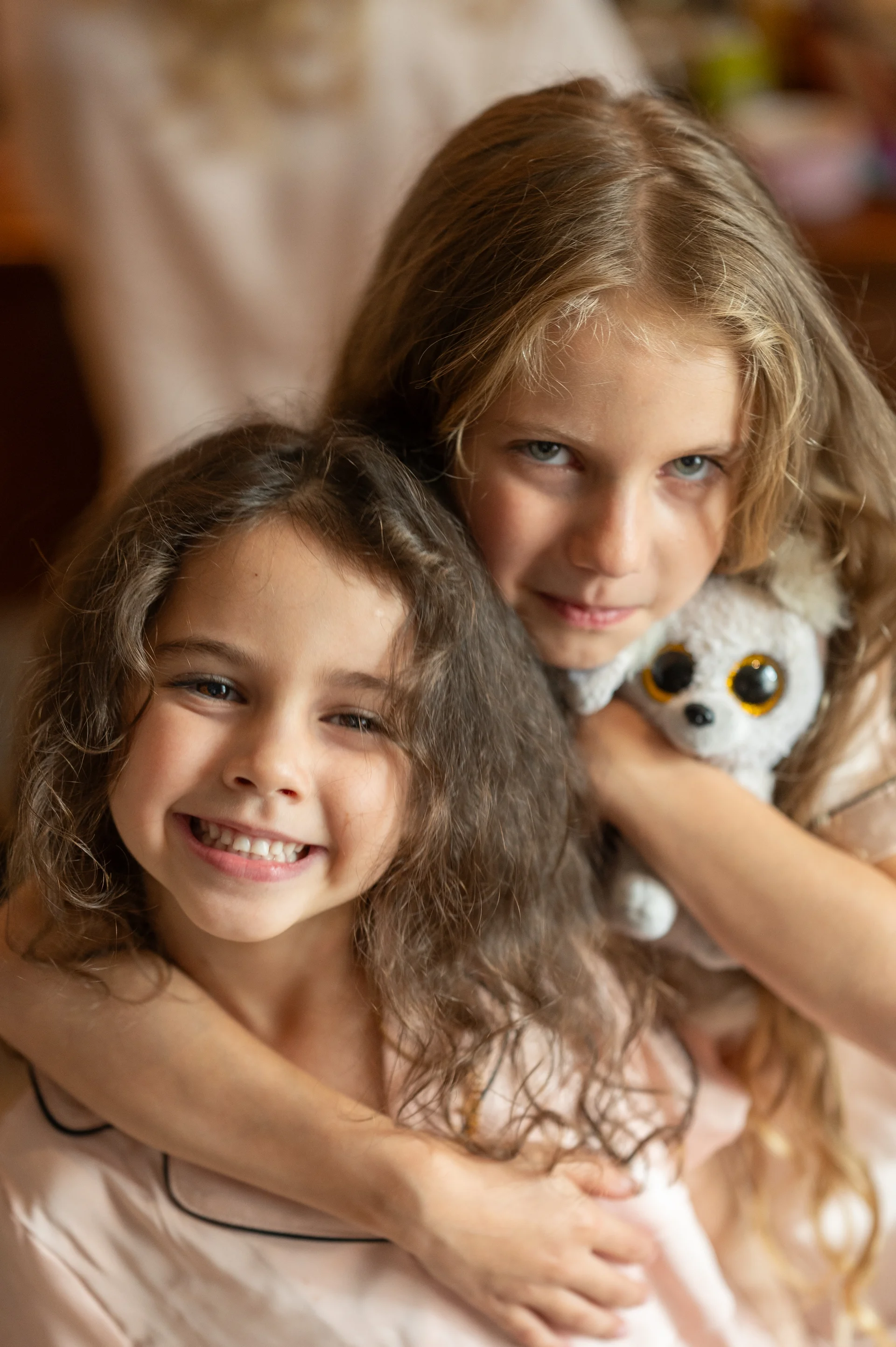 Two young flower girls wearing matching pyjamas share a joyful embrace while getting ready before the wedding ceremony.