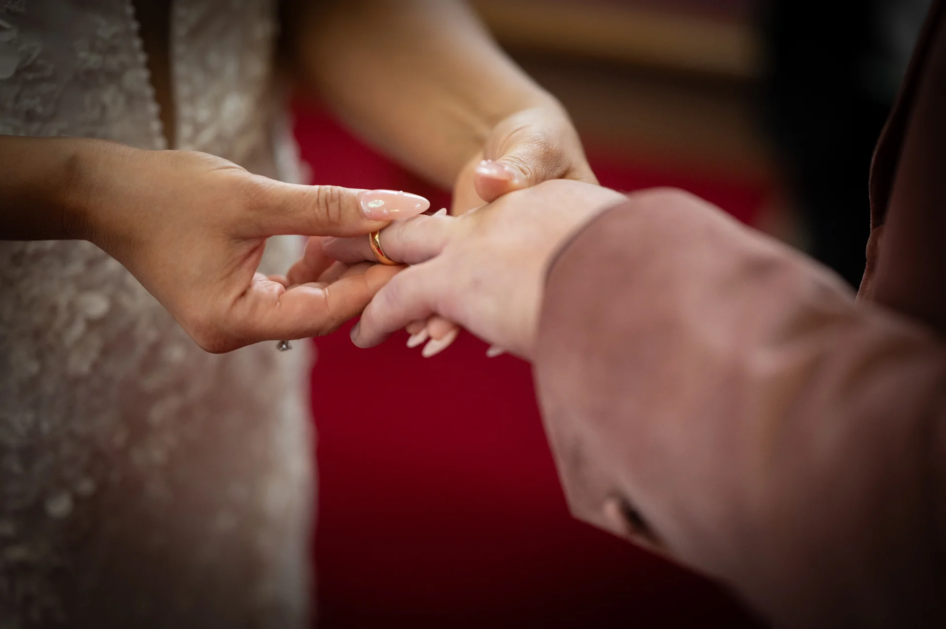 Close-up shot capturing a tender moment during the ceremony as a partner gently slides a gold wedding band onto the finger of the other.