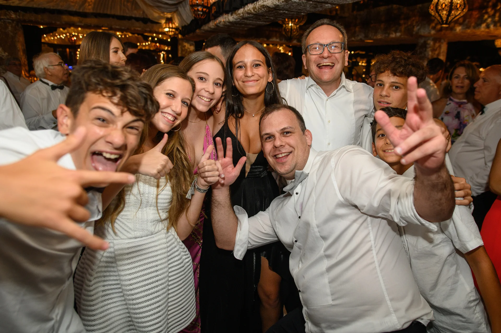 A joyful group of wedding guests laughing and posing excitedly together under direct flash lighting during the evening reception party.