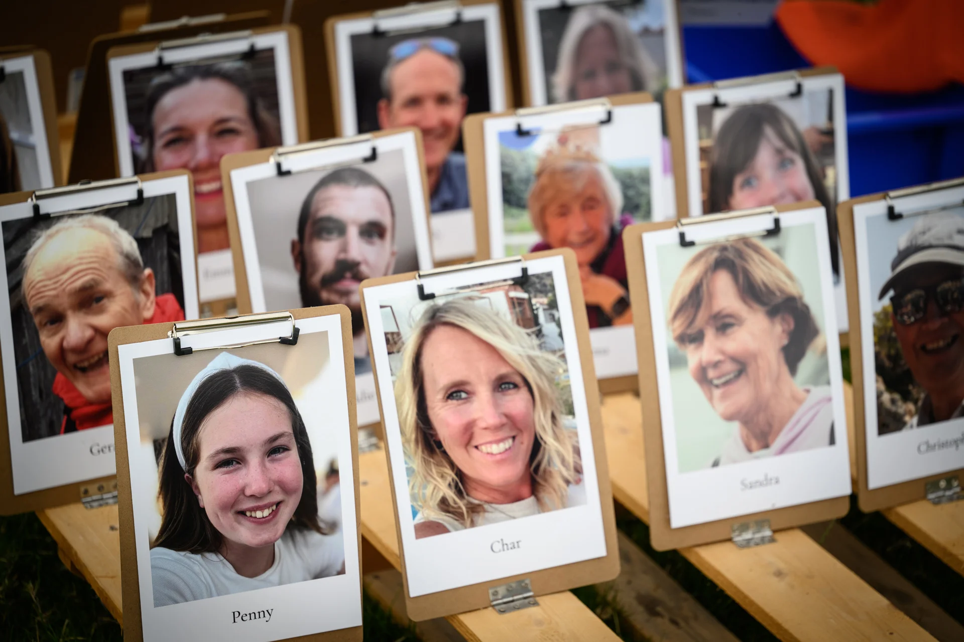 A creative and personal wedding photo display featuring smiling portraits of friends and family clipped onto individual wooden boards.