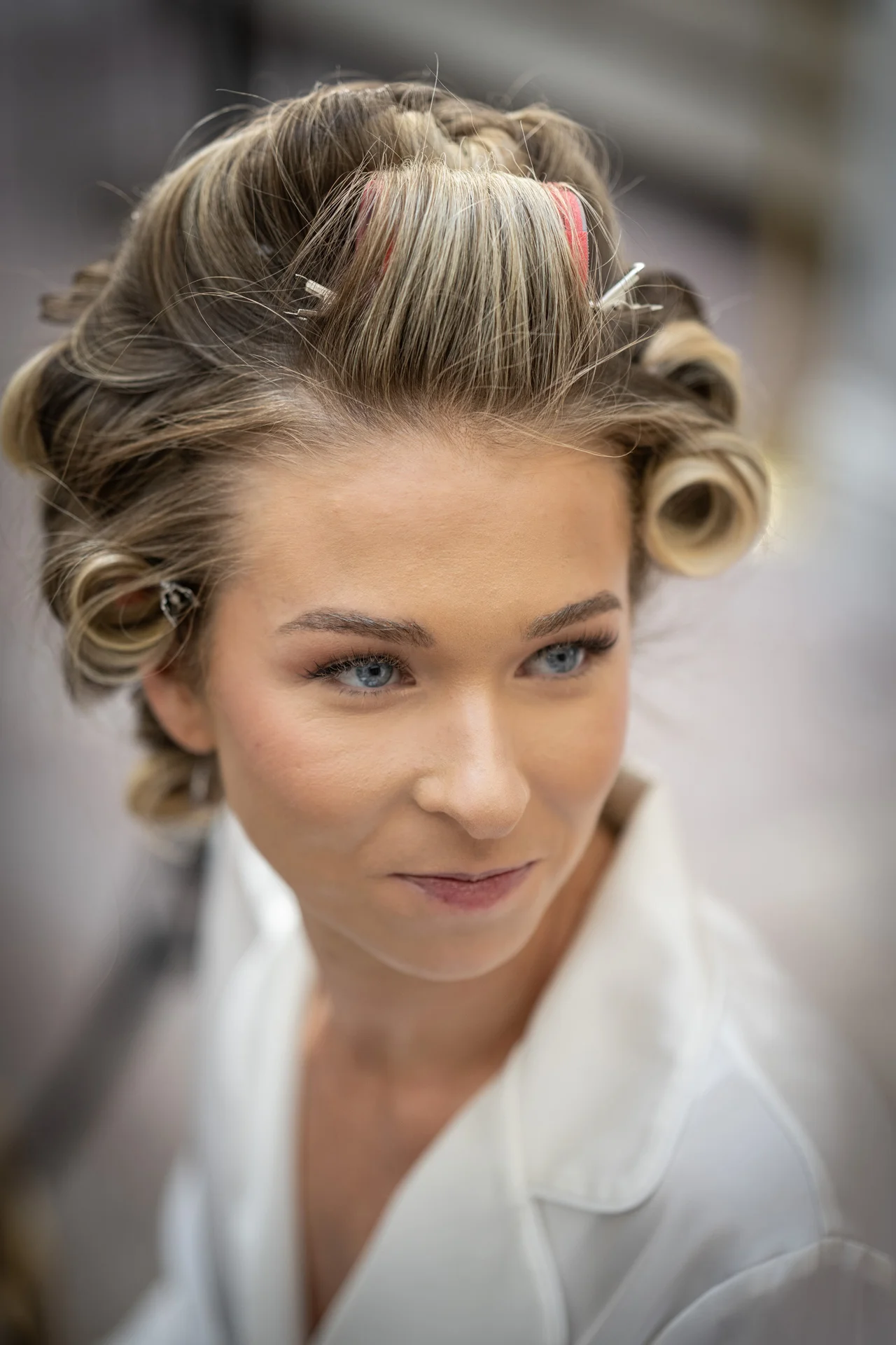A close up portrait of a bride during bridal prep with hair rollers in her blonde hair and wearing a white robe.