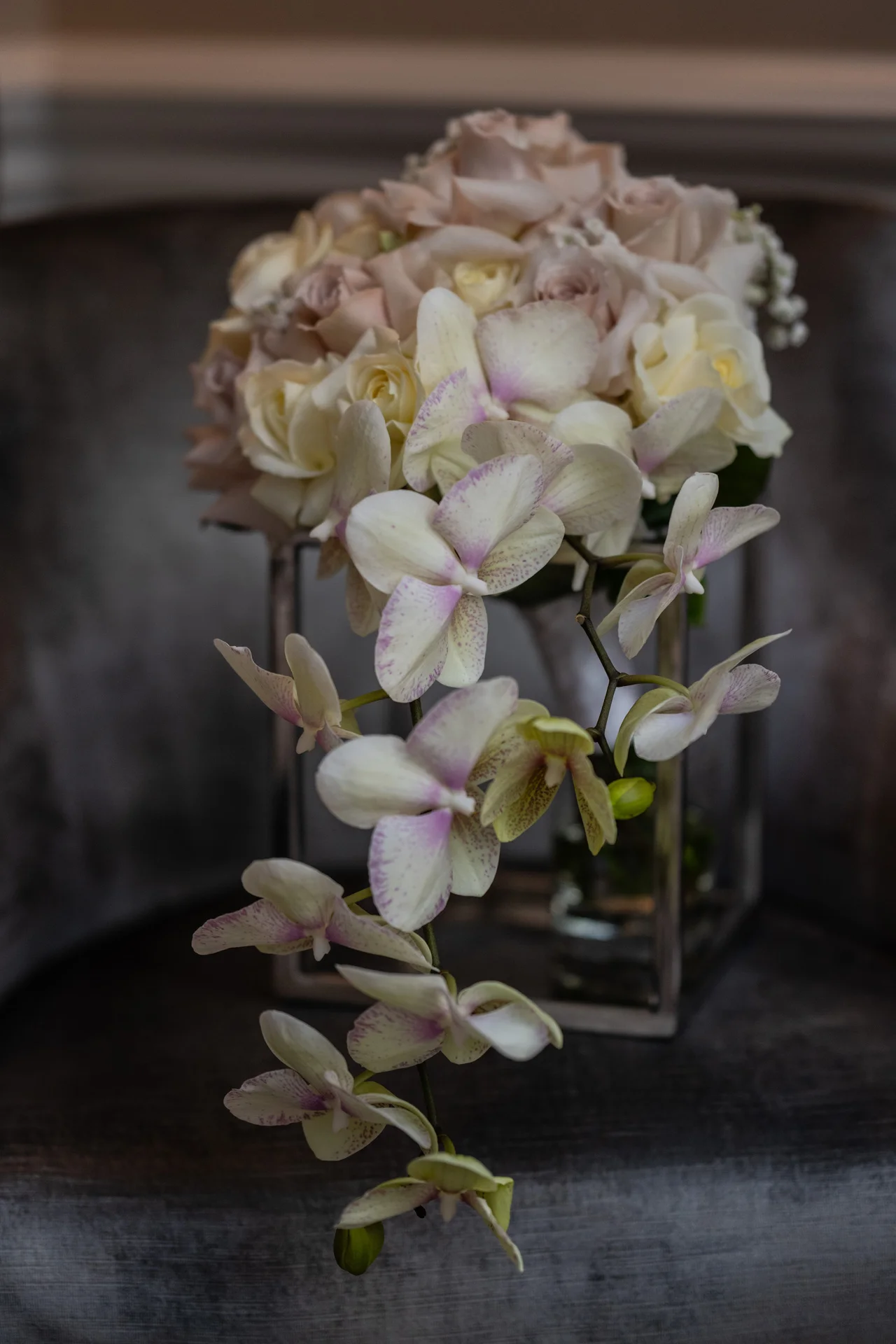 A cascading wedding bouquet featuring trailing speckled orchids and soft champagne roses rests elegantly on a metallic stand.