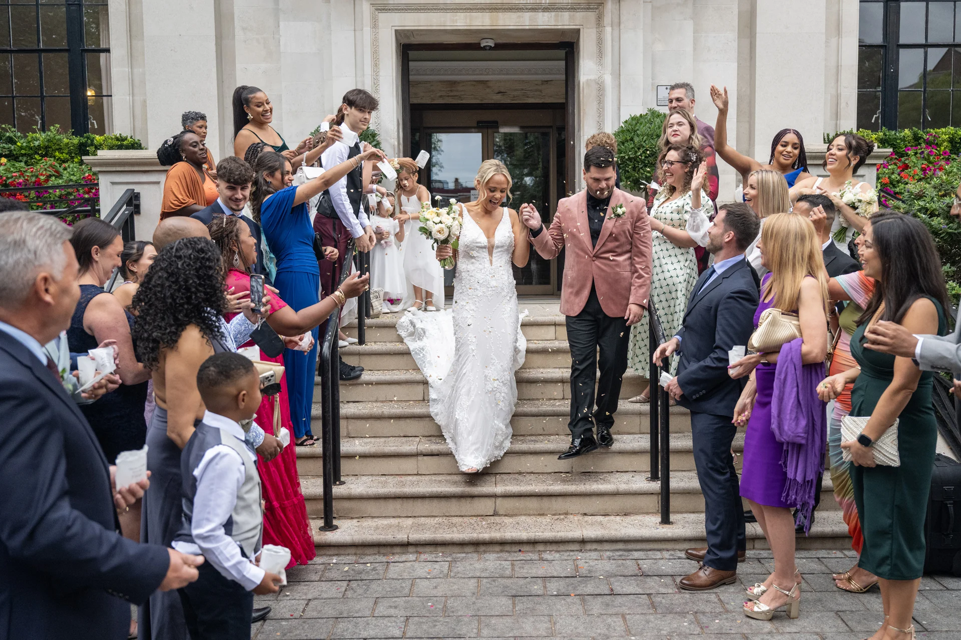 The joyful newlyweds descend the stone steps of a registry office hand in hand as cheering guests shower them with confetti.