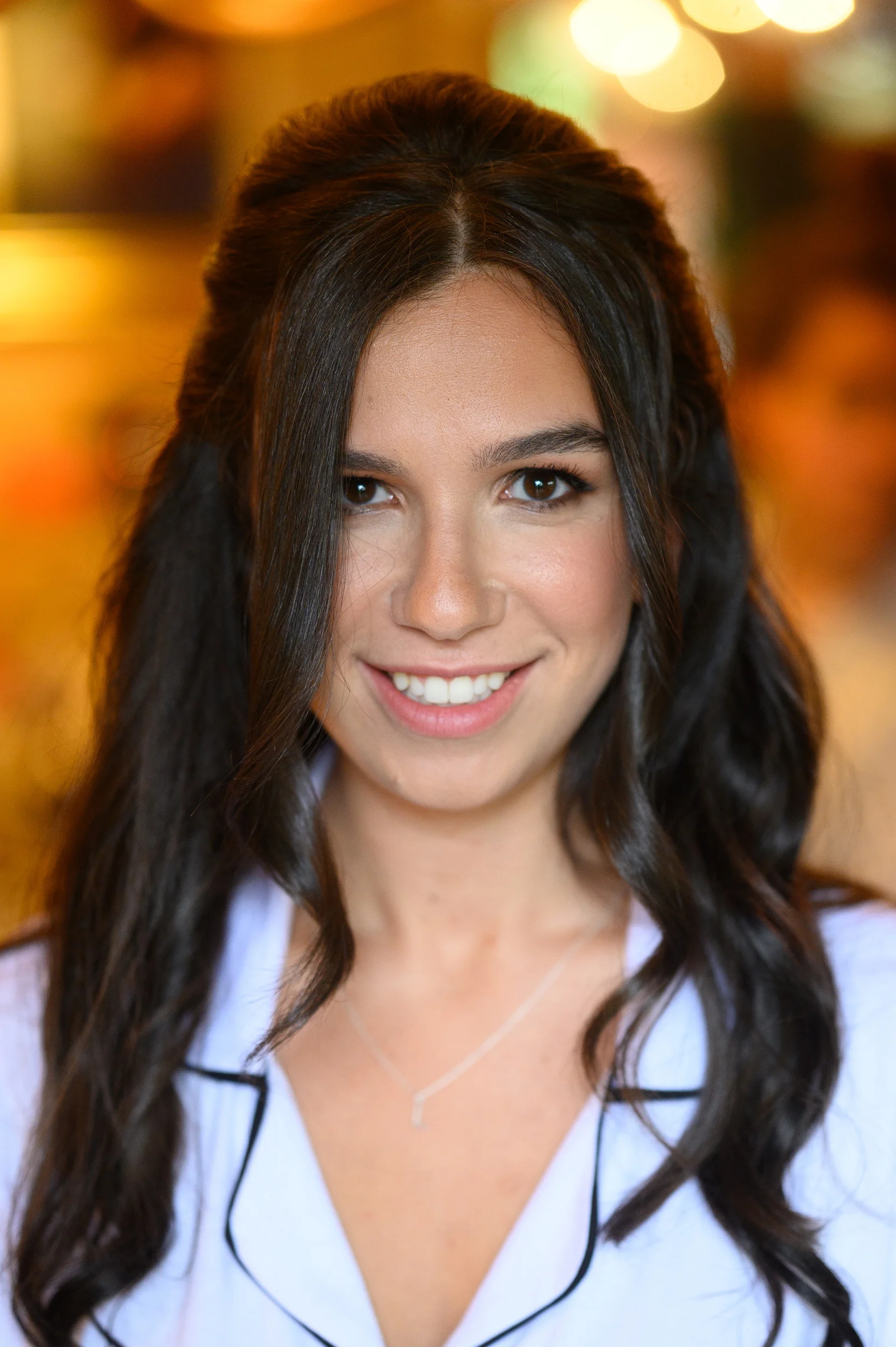 A close-up portrait of a smiling bride with dark hair styled half up and half down during bridal preparations.