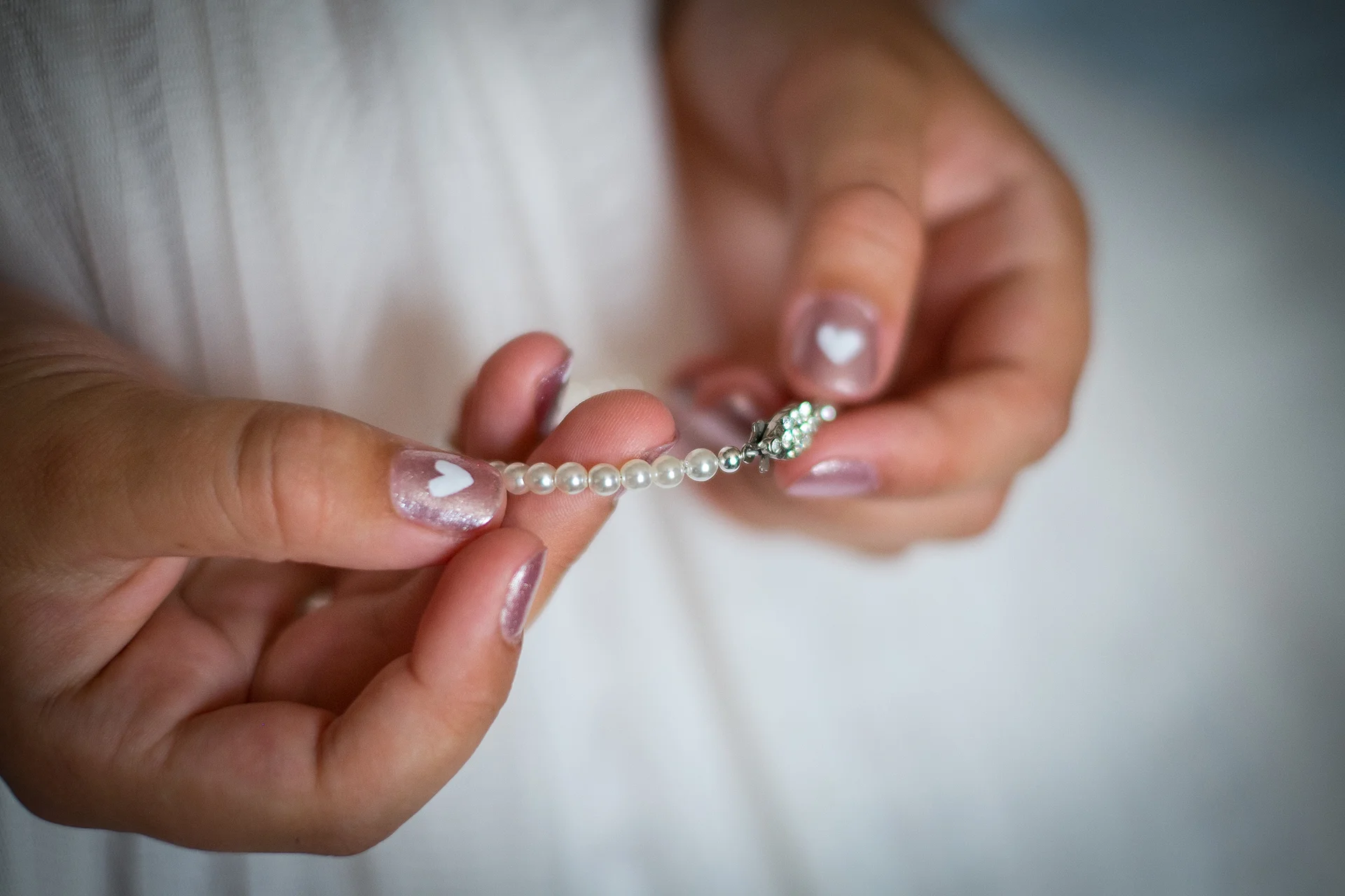 Close-up of hands wearing a delicate pearl bracelet with painted heart nail art during wedding preparations.