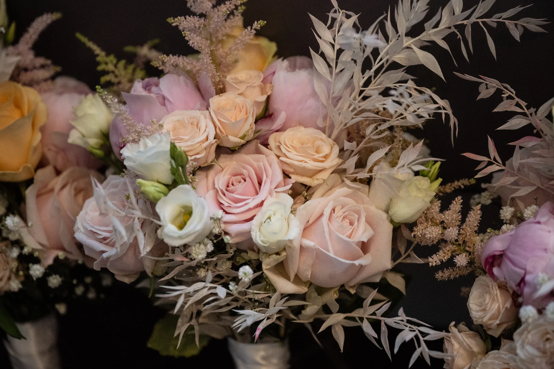 A close up view of a hand tied bridal bouquet featuring soft pink roses, cream lisianthus, fluffy peonies, and delicate bleached foliage.