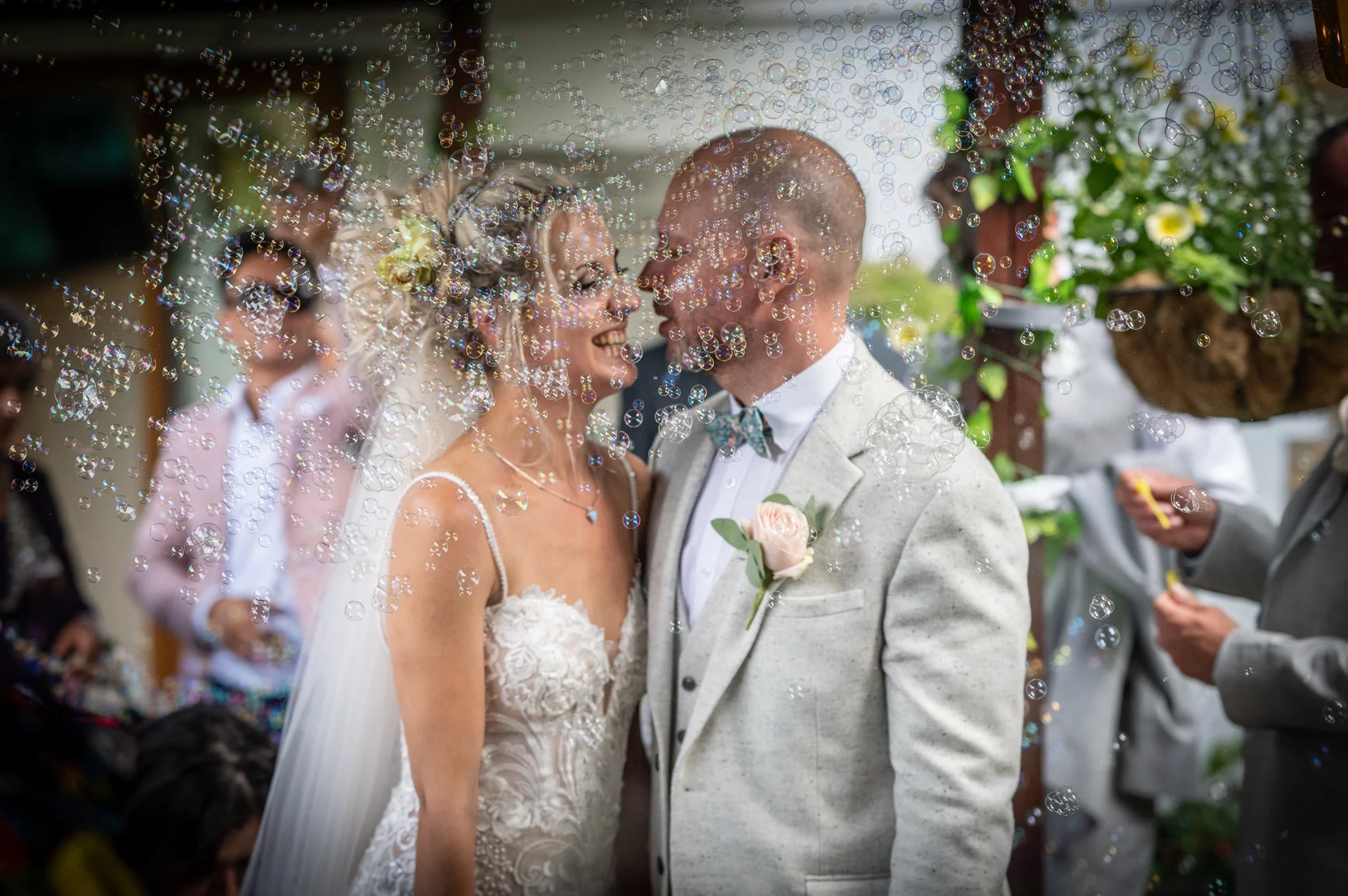 A newlywed bride and groom smile nose-to-nose as guests shower them with a playful cascade of floating bubbles after the ceremony.