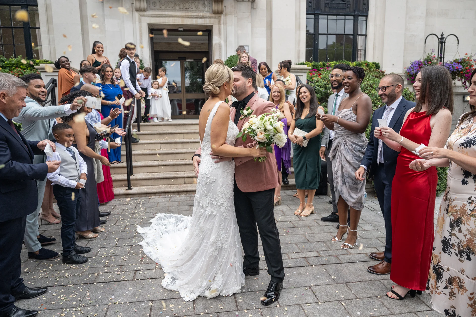 The newlyweds share a kiss outside a registry office as cheering wedding guests shower them with confetti.