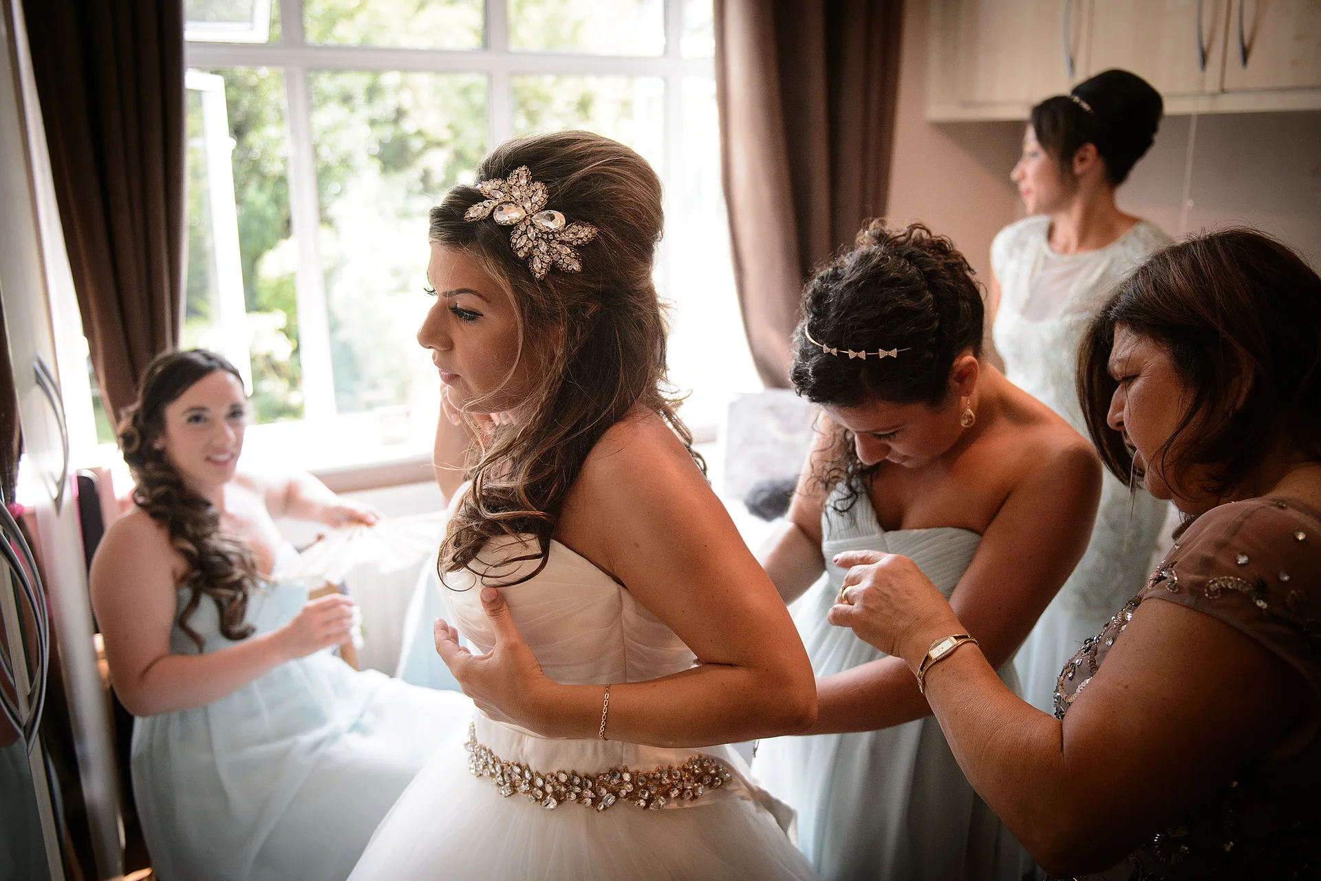 The bride is helped into her strapless white tulle wedding dress by her bridesmaids and mother during the morning preparations.