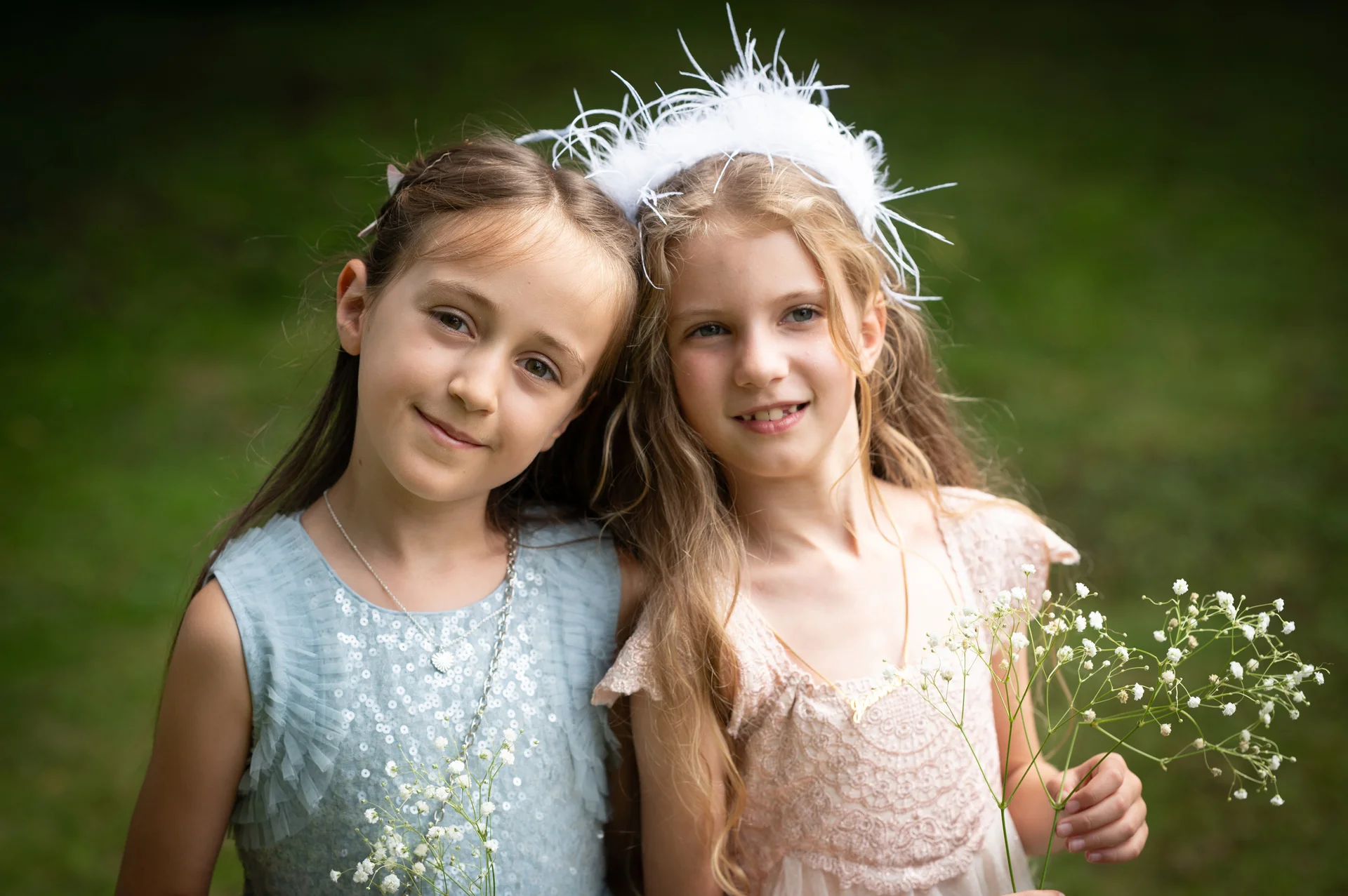 Two young flower girls posing together outdoors, wearing pastel dresses and holding delicate stems of baby's breath.